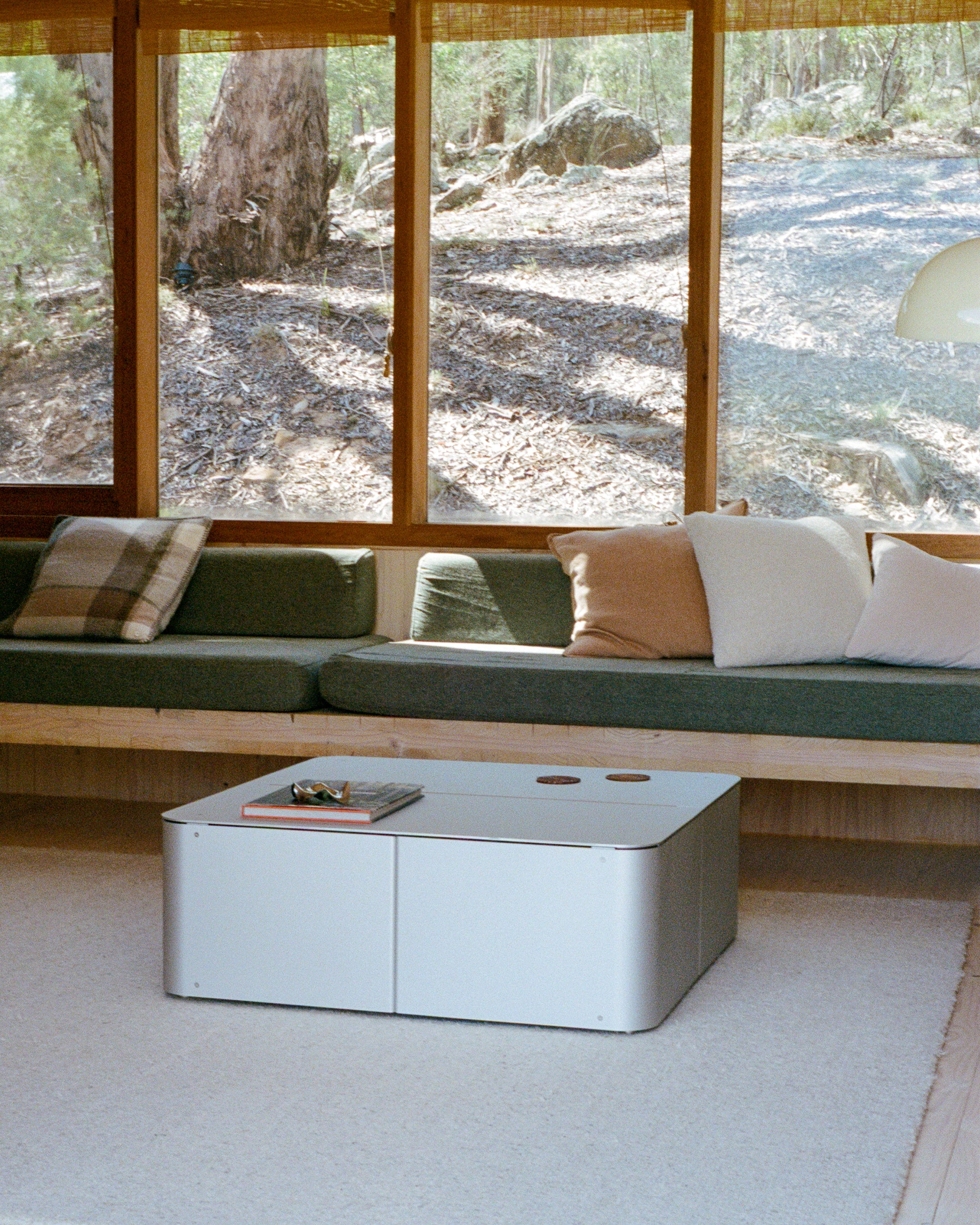 Coffee Table by PARCTA in a living area in a wood cabin on a neutral rug with a green sofa. There's large windows in the background showing woodland.