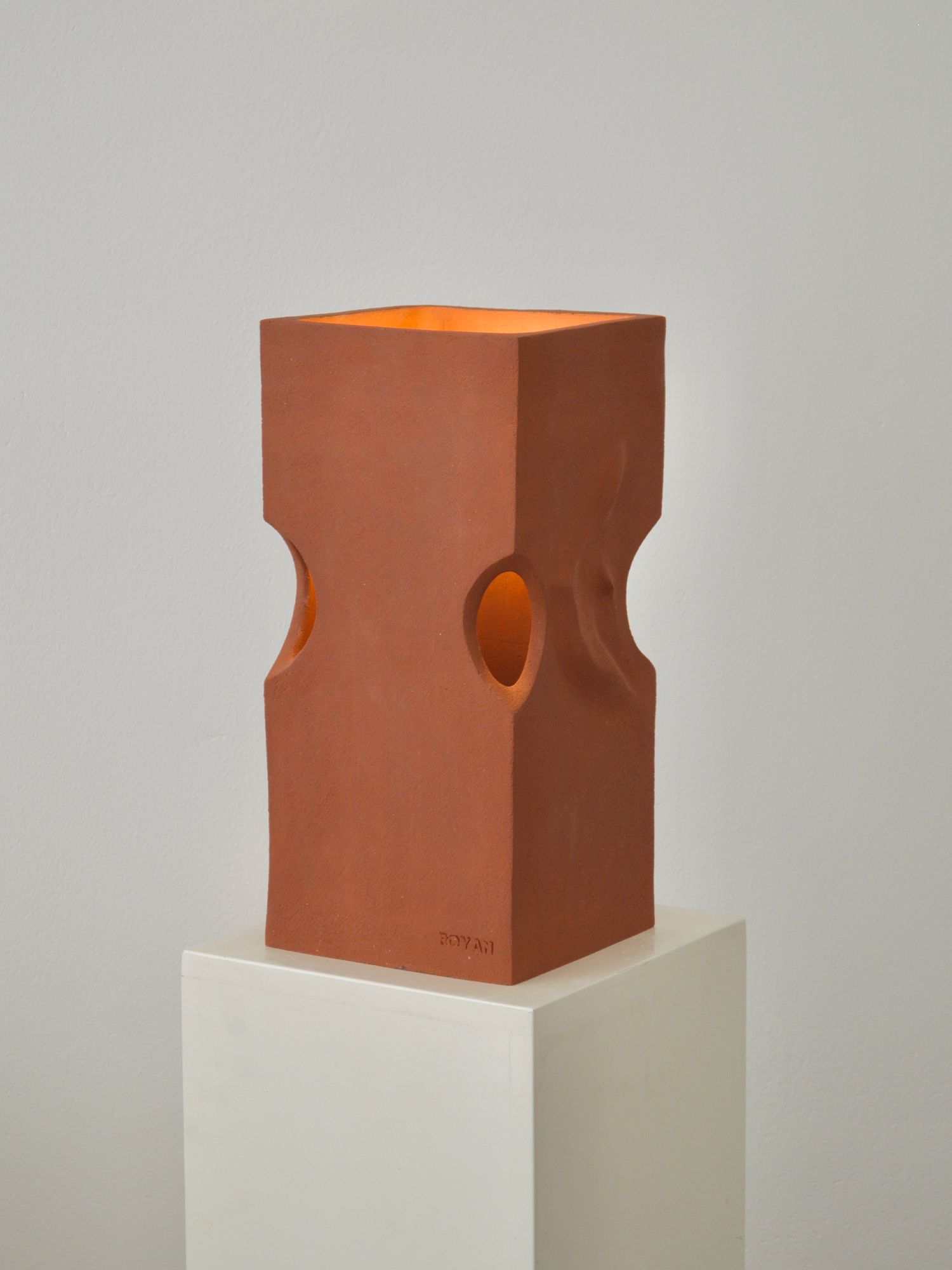 Ceramic lamp by Zeynep Boyan sat on a white plinth with the light on.