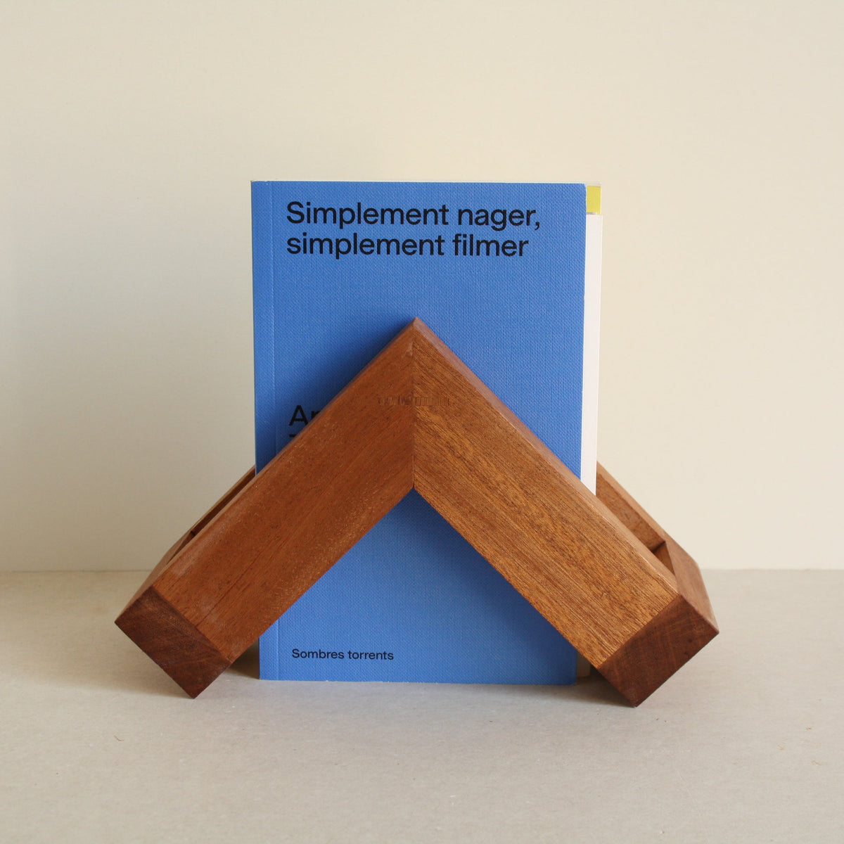 A multipurpose wooden bookend by Evelyn Vanoverbeke holding books on a neutral background.