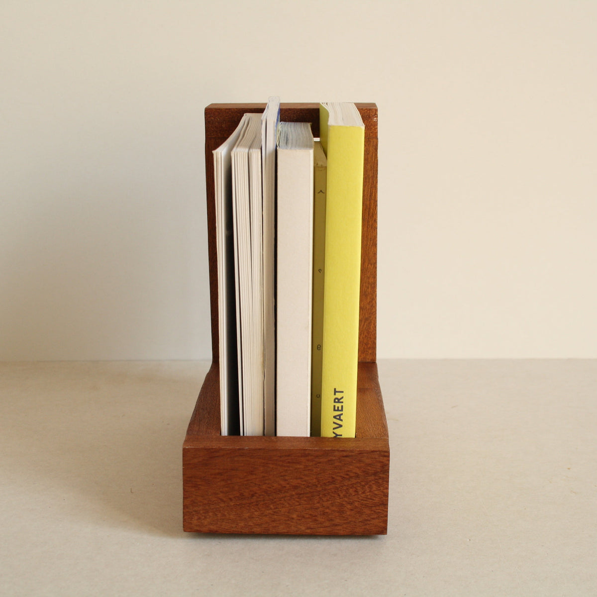 A multipurpose wooden bookend by Evelyn Vanoverbeke holding books on a neutral background.