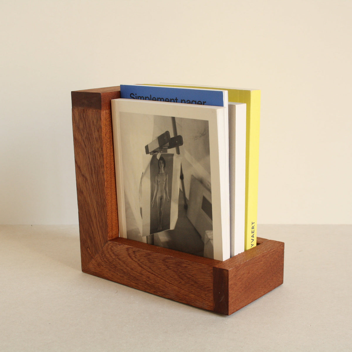 A multipurpose wooden bookend by Evelyn Vanoverbeke holding books on a neutral background.