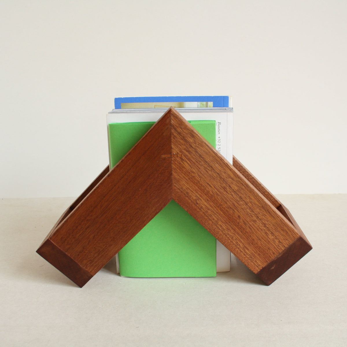 A multipurpose wooden bookend by Evelyn Vanoverbeke holding books on a neutral background.