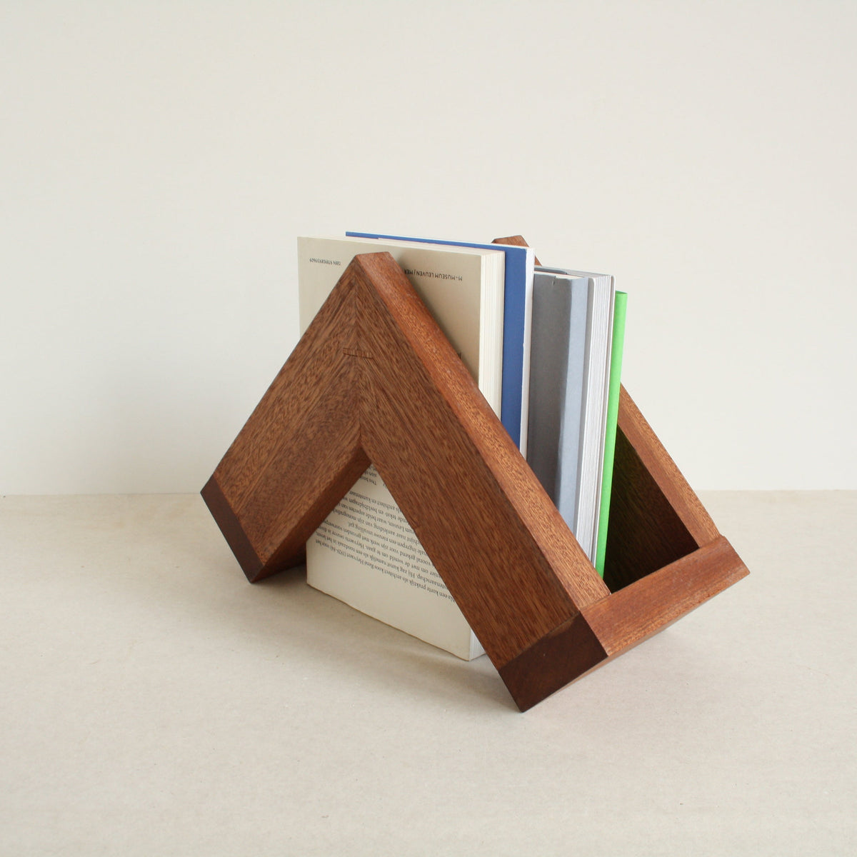 A multipurpose wooden bookend by Evelyn Vanoverbeke holding books on a neutral background.