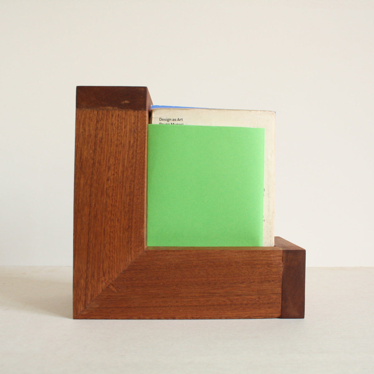 A multipurpose wooden bookend by Evelyn Vanoverbeke holding books on a neutral background.