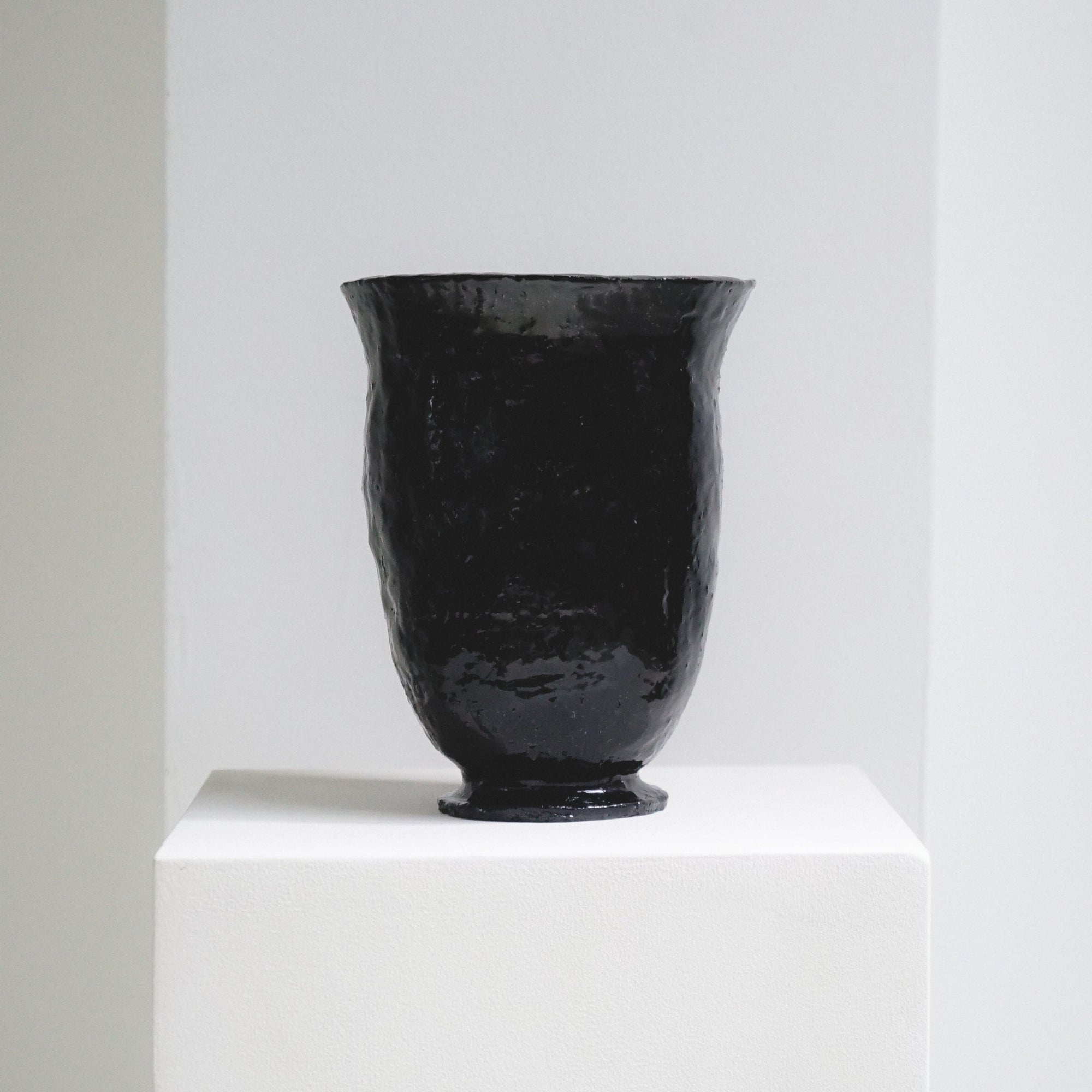 Black, glossy ceramic chalice vase by klangnapha on a white plinth with a neutral background.