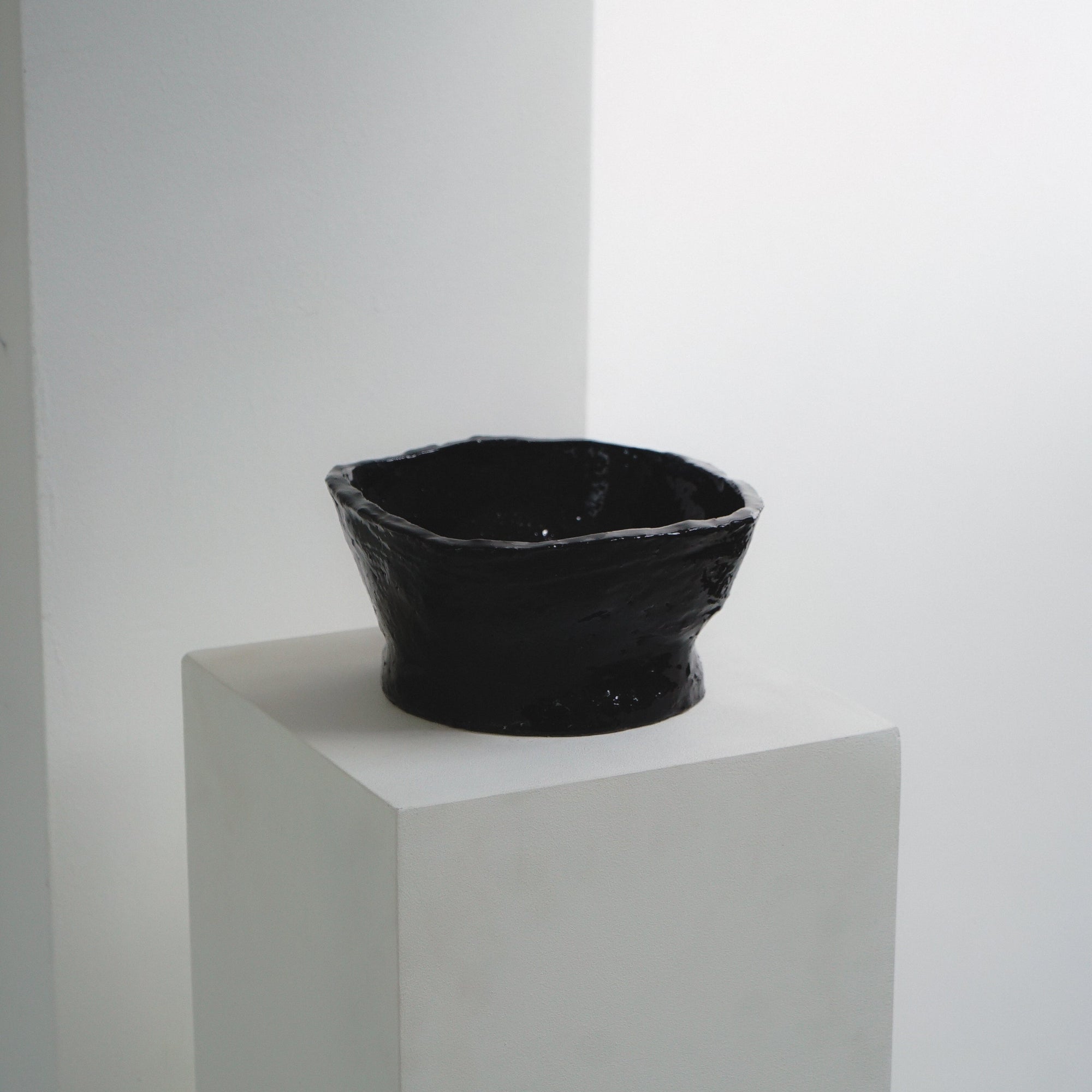 Square ceramic bowl by klangnapha in a dark gloss, sat on top of a white plinth on a white background.
