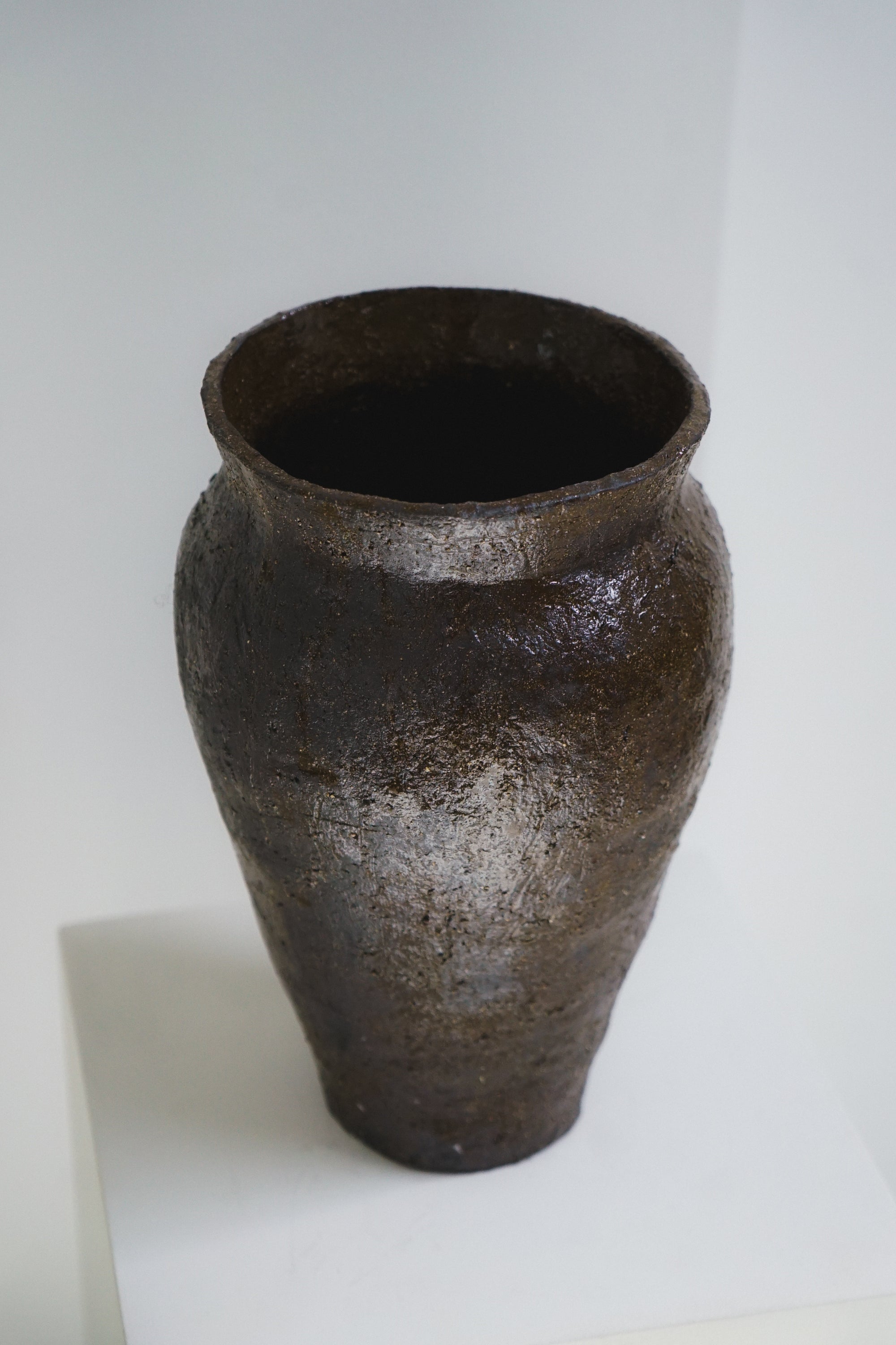Textured brown ceramic vase by klangnapha on a white plinth against a neutral background.