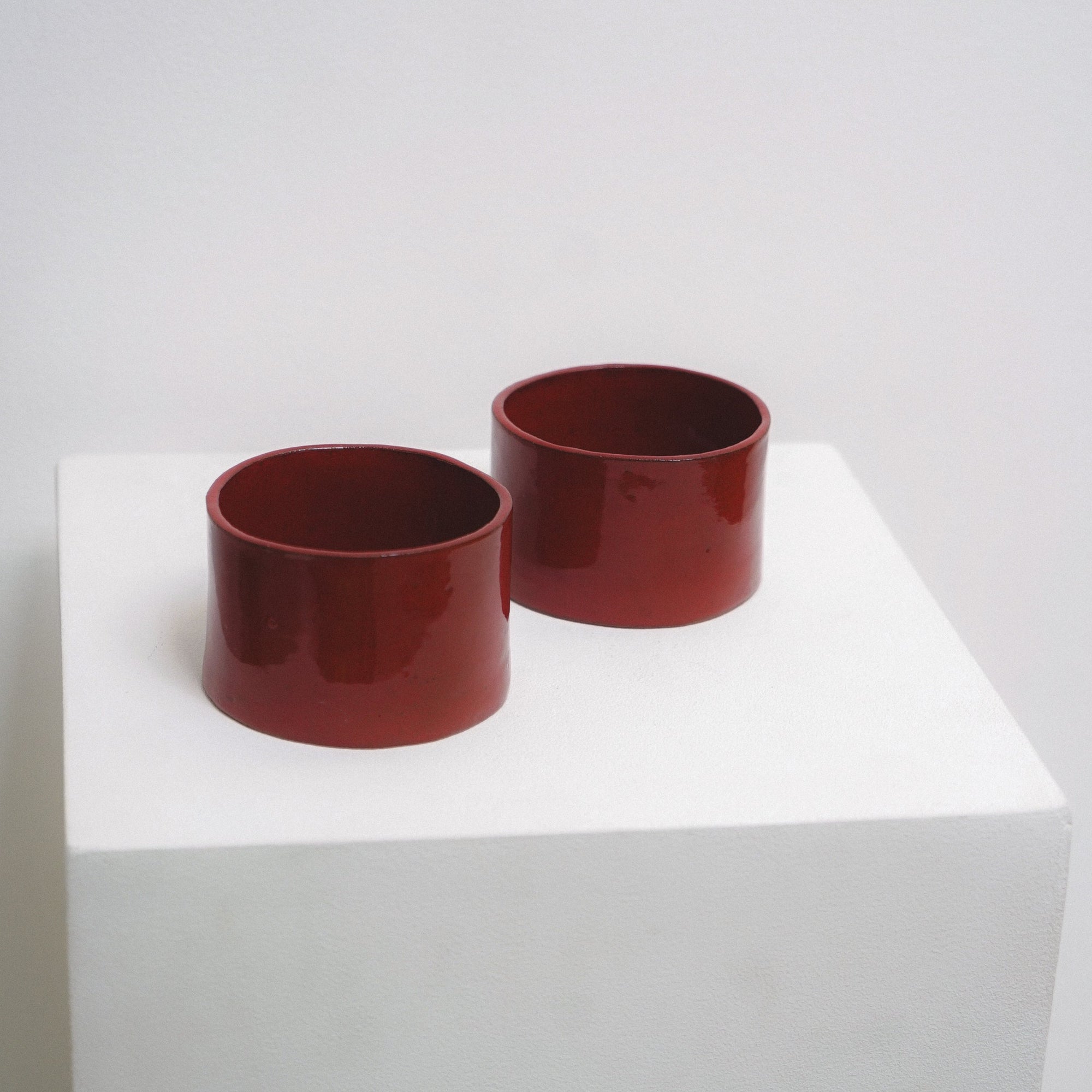 Two, red, glossy ceramic coffee cups by klangnapha on a white plinth with a white background.