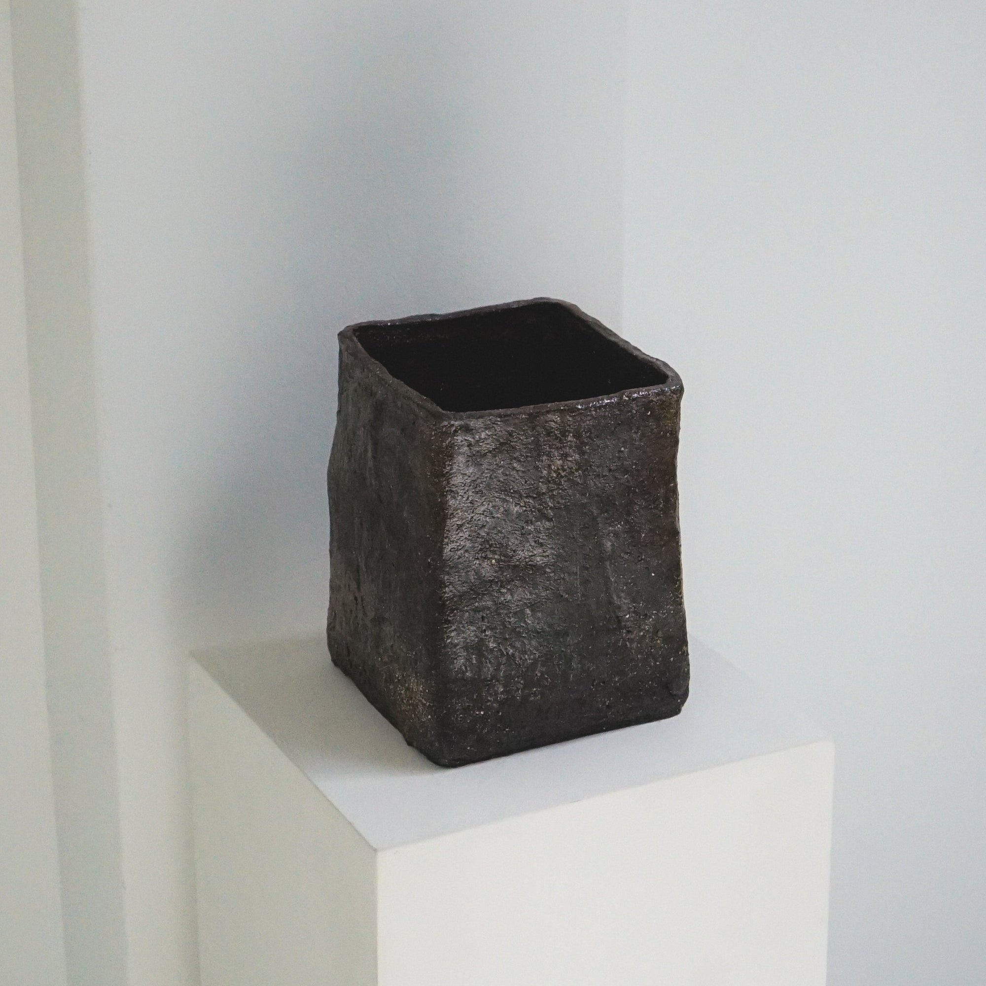 Textured, charcoal cubed vase by klangnapha on a white plinth with a neutral background.