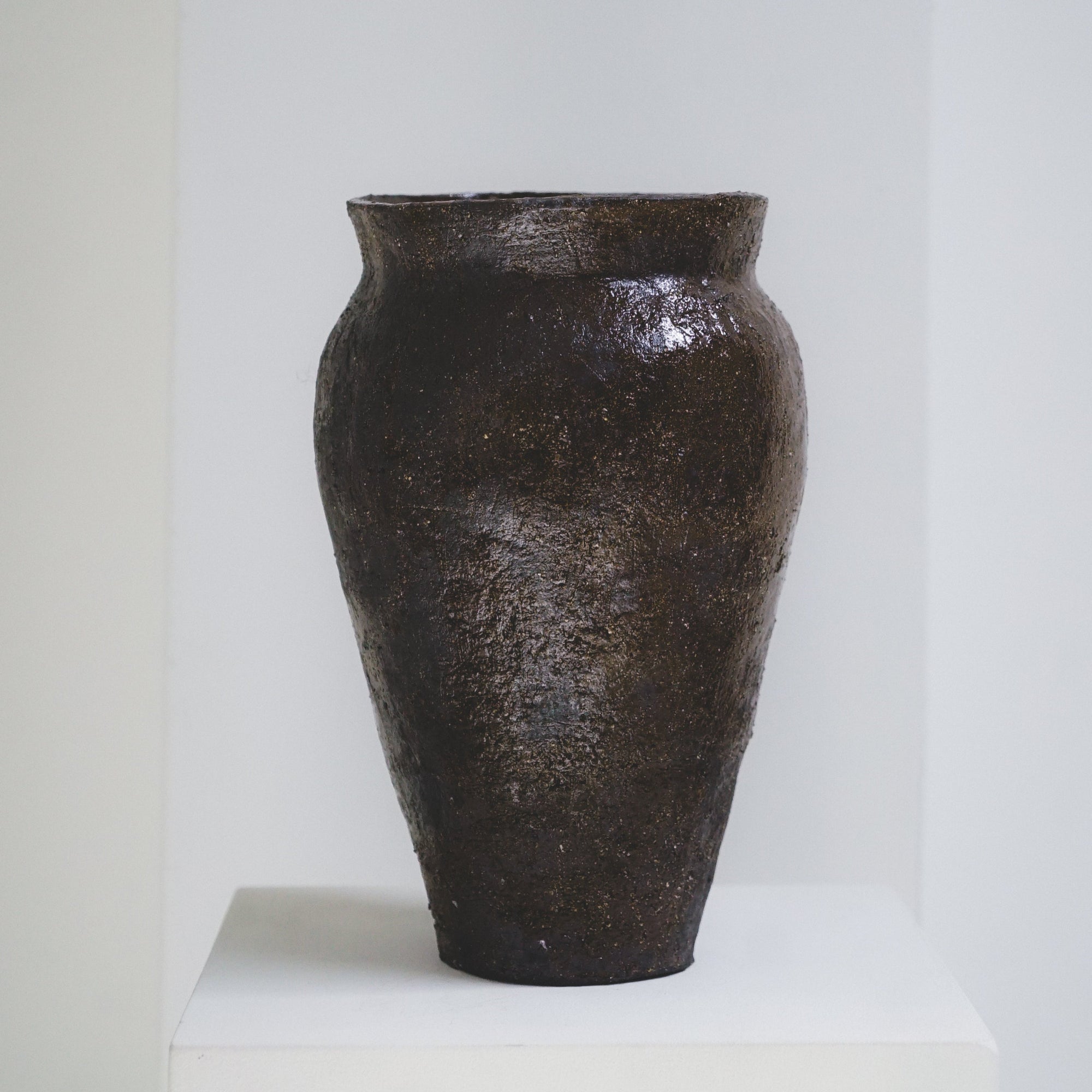 Textured brown ceramic vase by klangnapha on a white plinth against a neutral background.