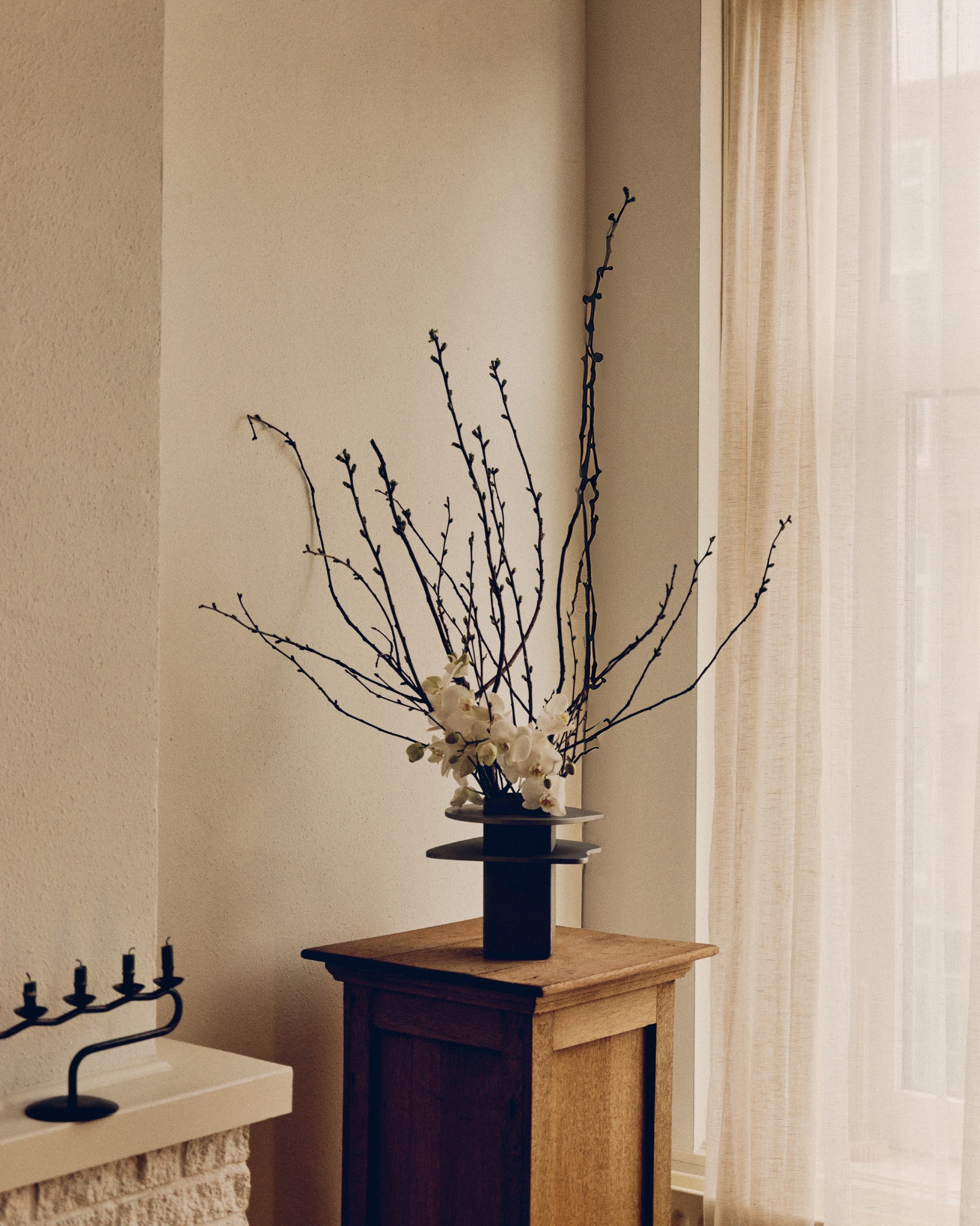 Vase by PARCTA with decorative arrangement of branches and flowers on a wooden table against a beige wall.