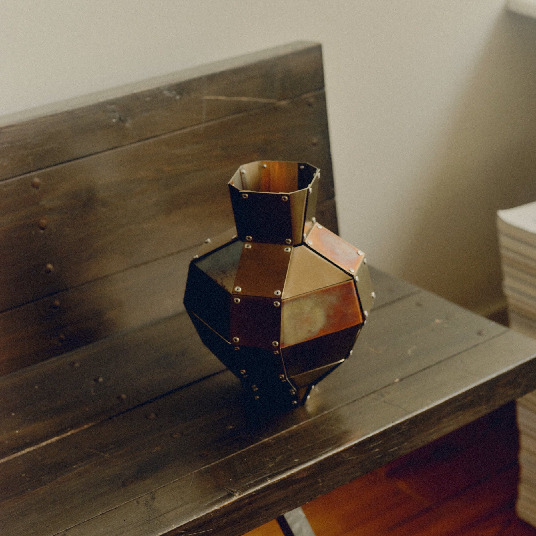 Stainless steel and copper decorative object by Theo Galliakis sat on wooden bench besides a stack of magazines.