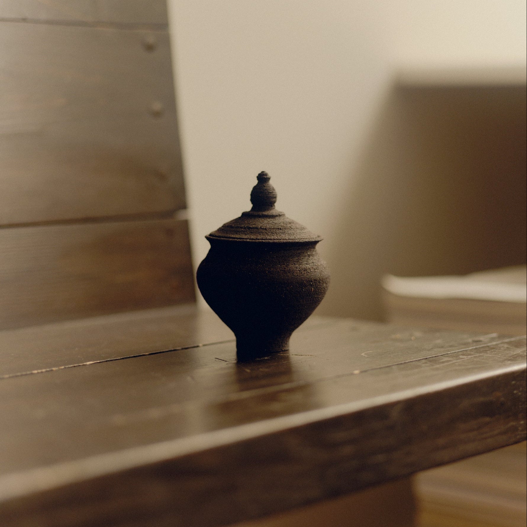 Small textured ceramic jar with a lid by Bastian Bjerge sat on a wooden bench.