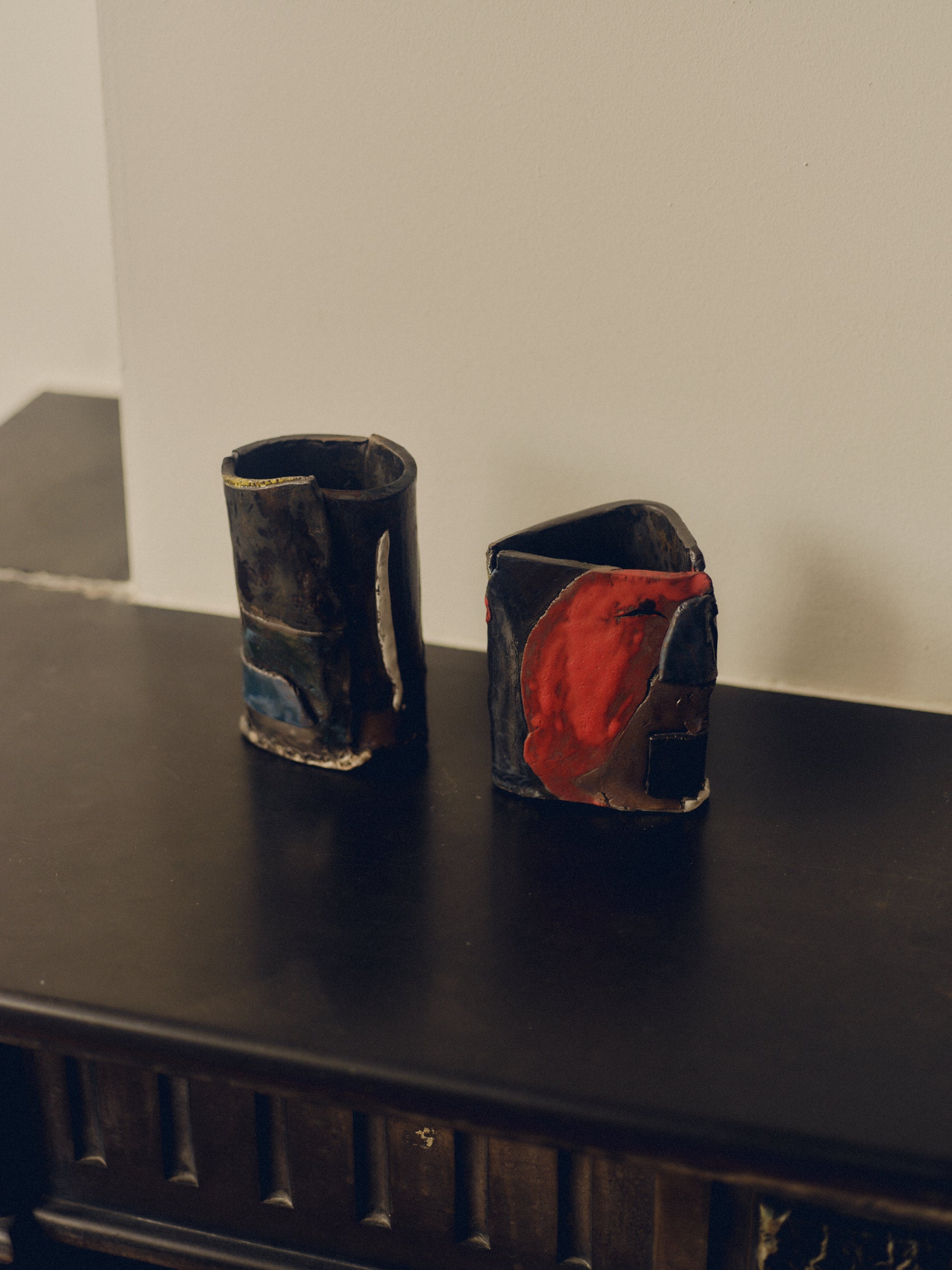 Set of two patchwork ceramic objects with abstract designs by May Liok sat on top of a decorative fireplace.