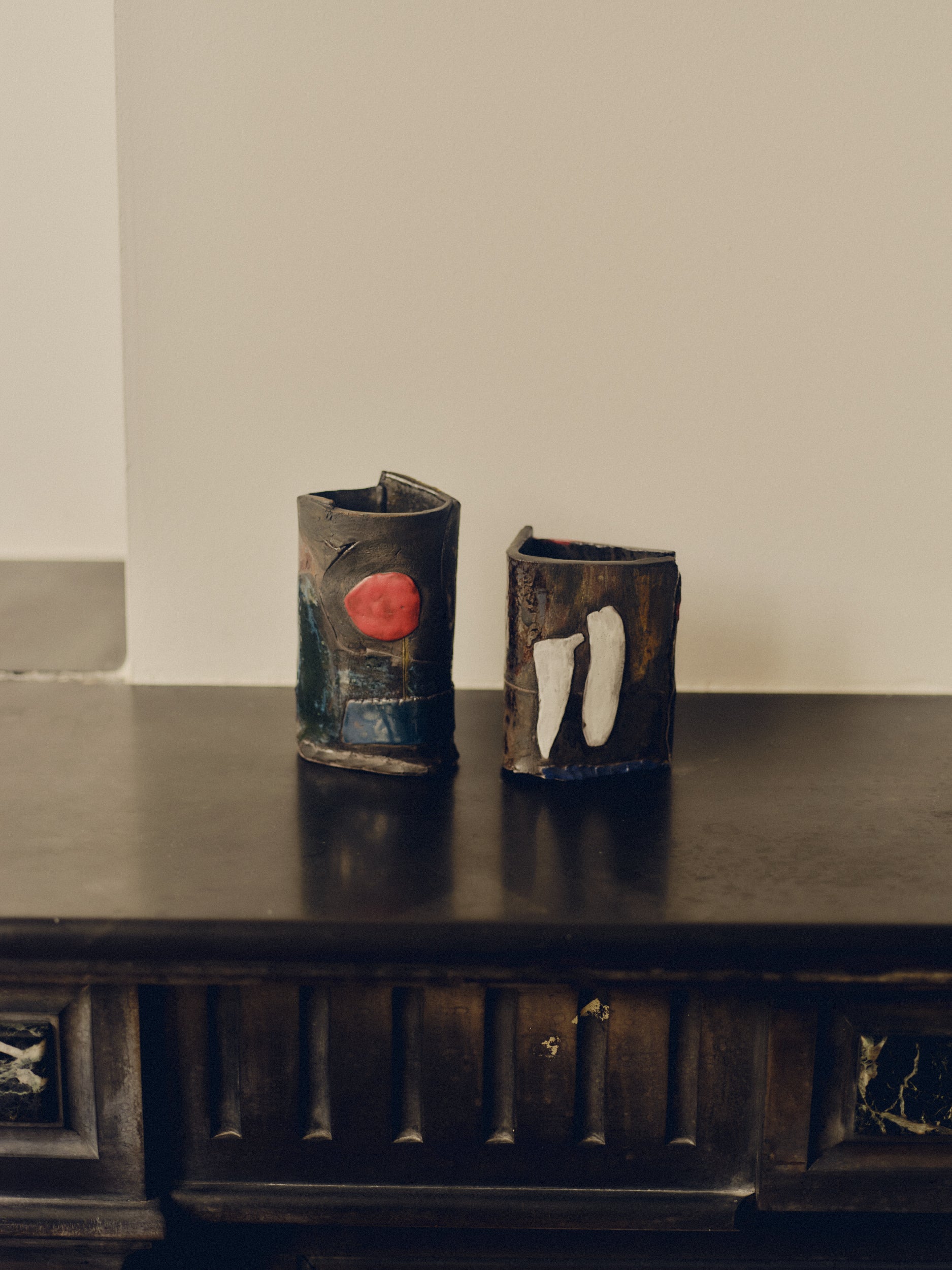 Set of two patchwork ceramic objects with abstract designs by May Liok sat on top of a decorative fireplace.