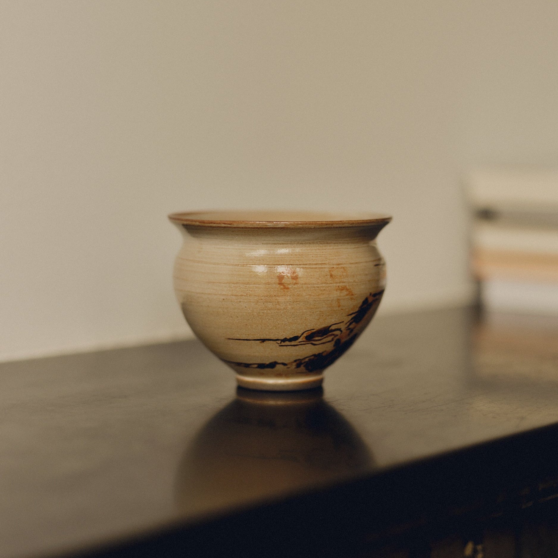 Cream ceramic decorative bowl by Bastian Bjerge with brown hand painted design on a fire place surface with blurred books in the background.