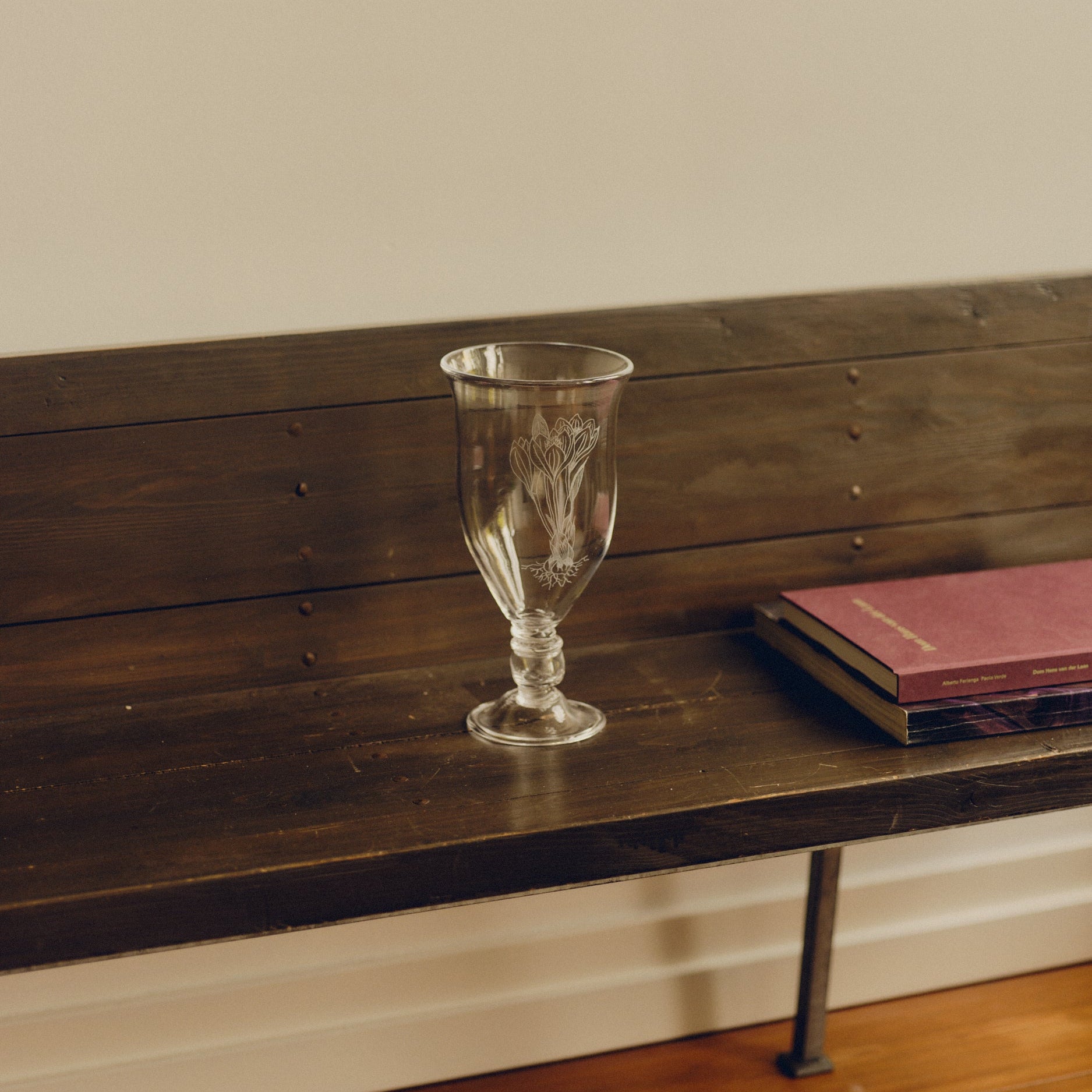 Glass vase with engraved floral decoration by Bastian Bjerge sat on a bench with two books besides it.