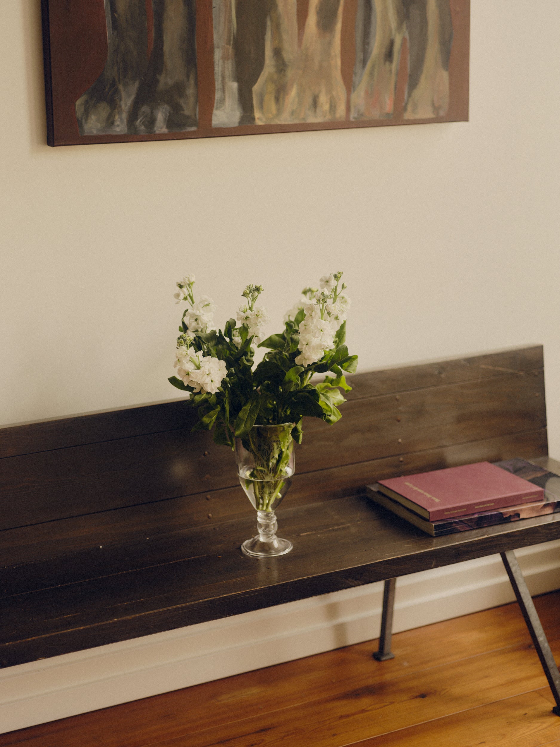 Glass vase with engraved floral decoration by Bastian Bjerge holding flowers, sat on a bench with two books besides it and a painting hanging above.