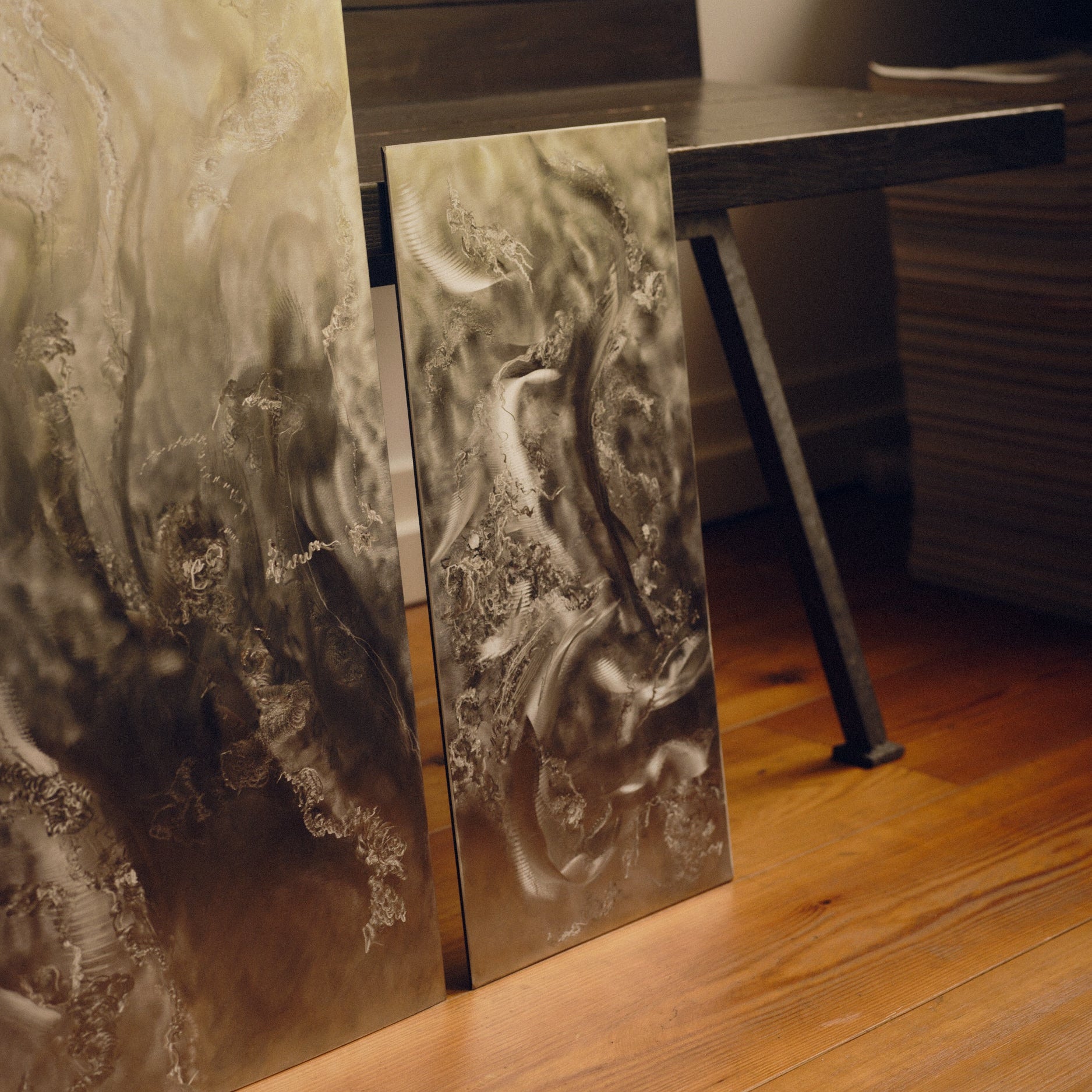 Engraved stainless steel wall art by Grace Houghton, in sizes small and medium, leaning against a wooden bench on a wooden floor.