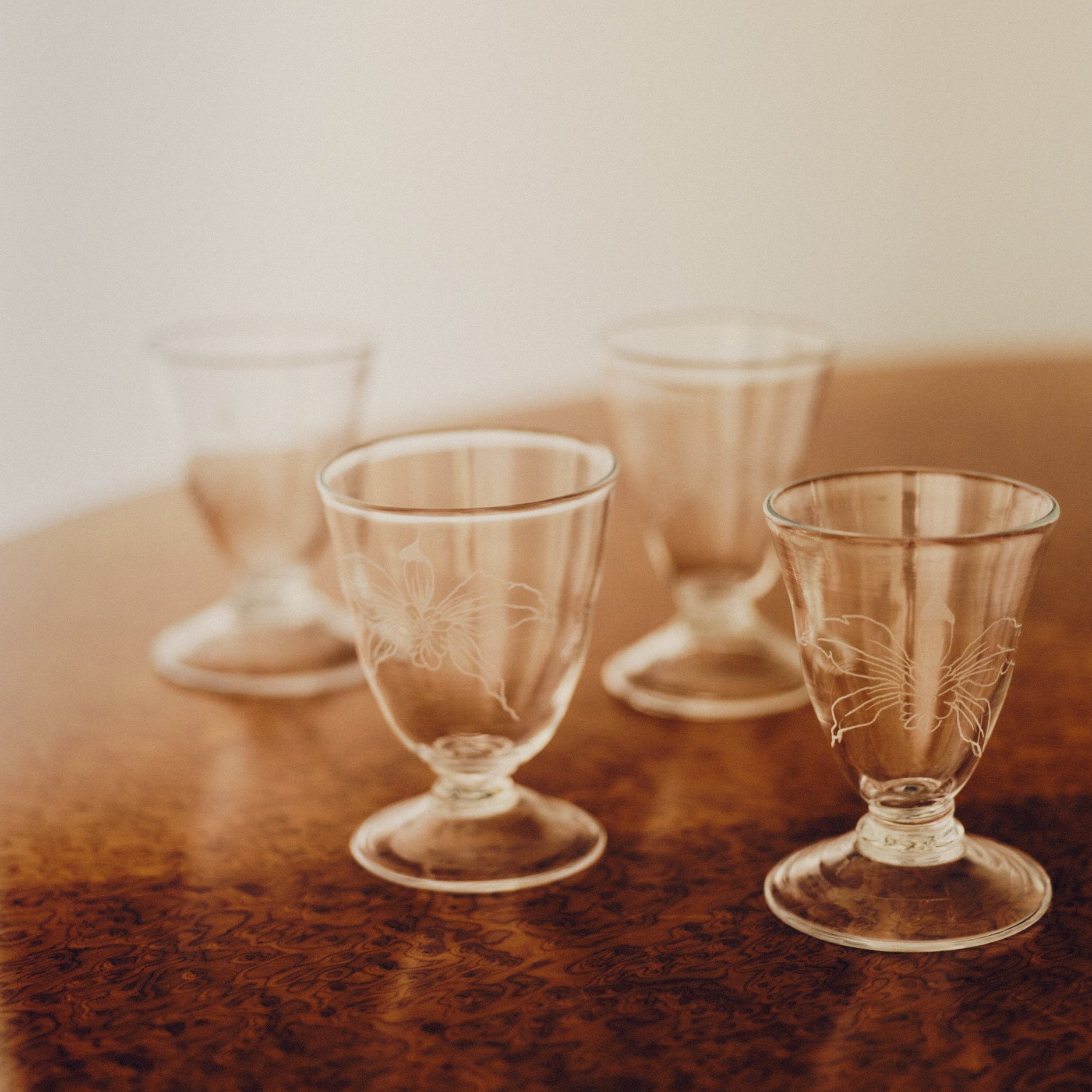 Four wine glasses with engraved flowers by Bastian Bjerge sat on a burl wood table.