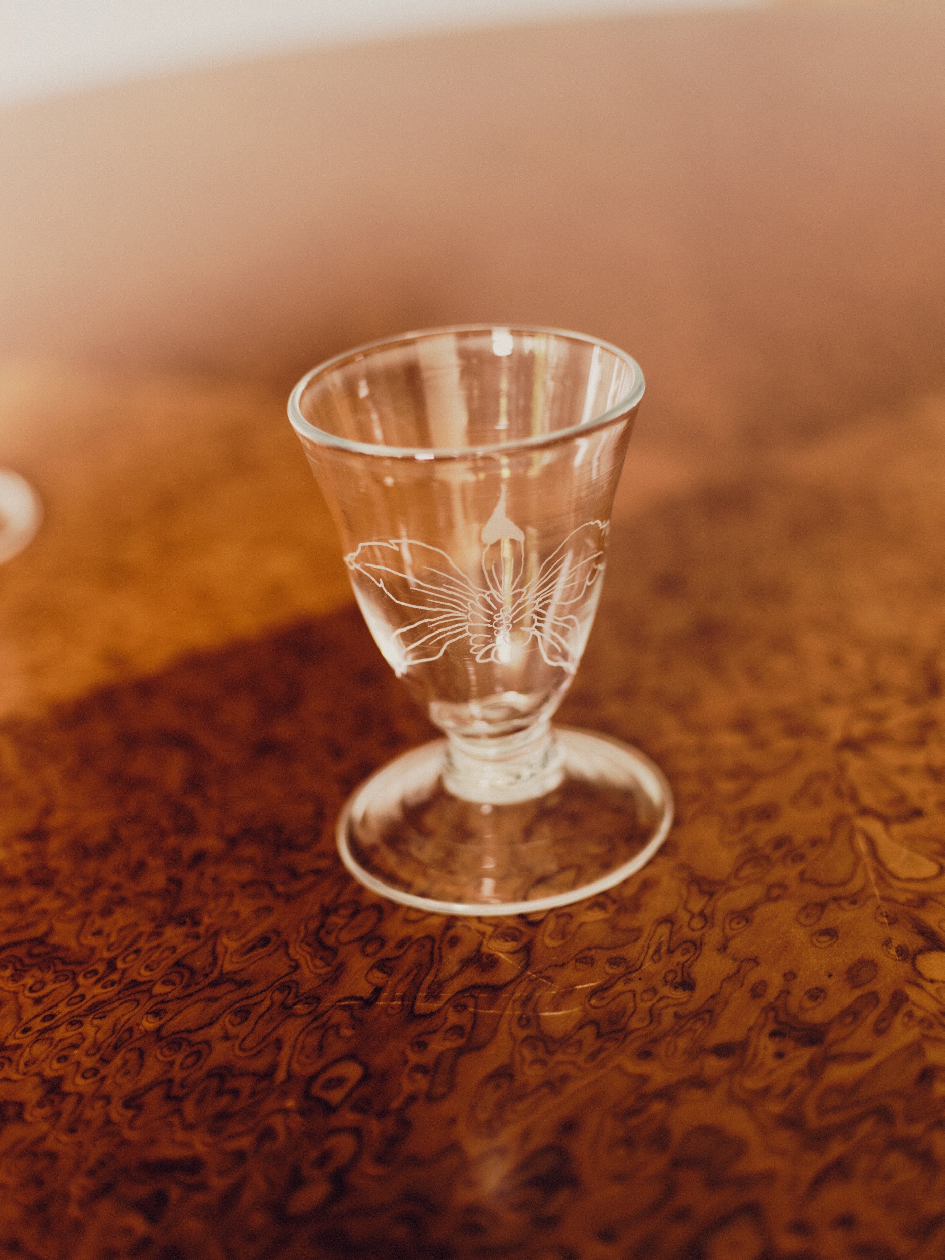 Floral engraved wine glass by Bastian Bjerge on a burl wood table.