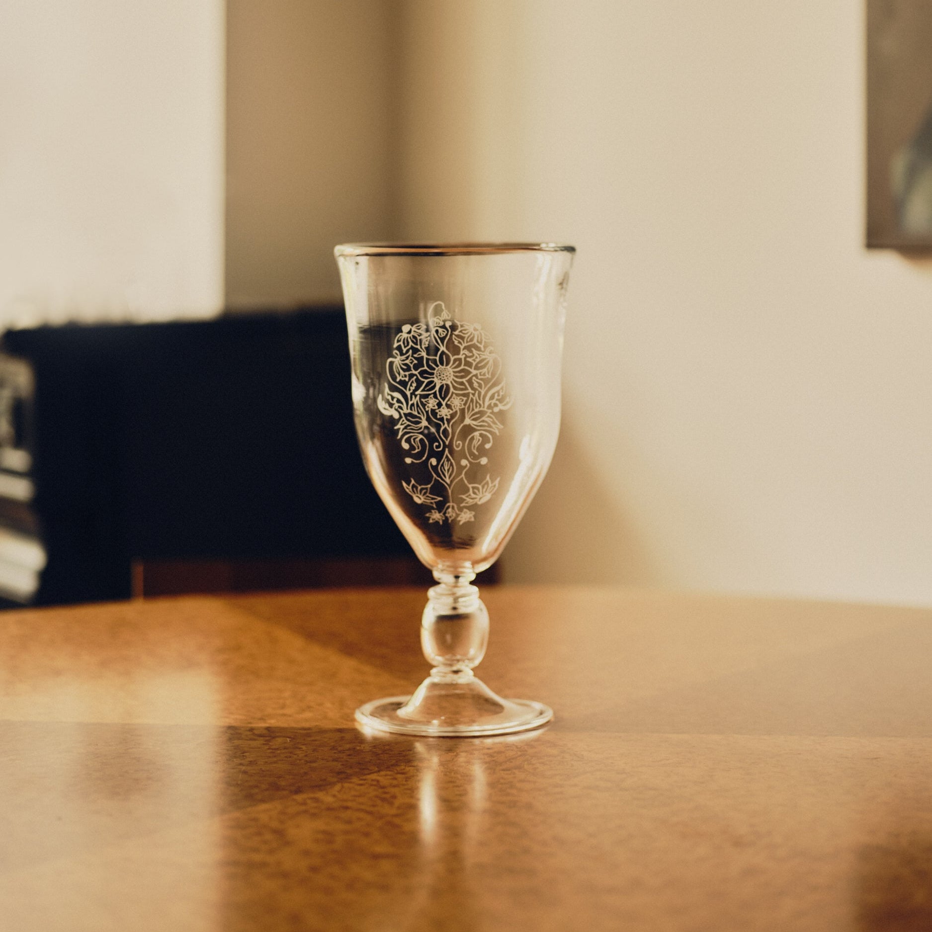 Glass vase with an engraved floral decoration by Bastian Bjerge sat on a burl wood table with a blurred fireplace in the background.