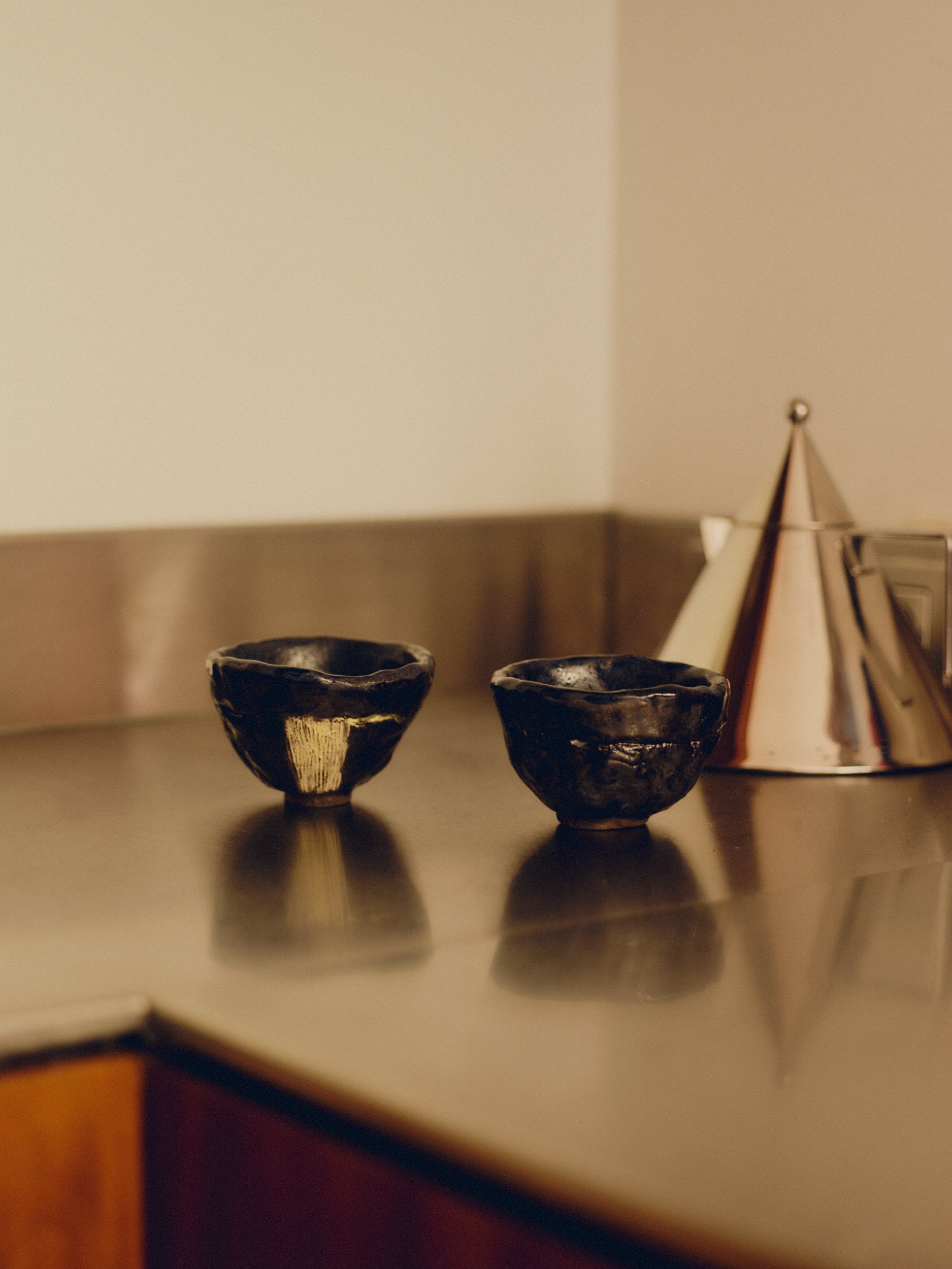 Set of two black and yellow ceramic tea cups by May Liok on a stainless steel kitchen countertop with a stainless steel kettle in the background.