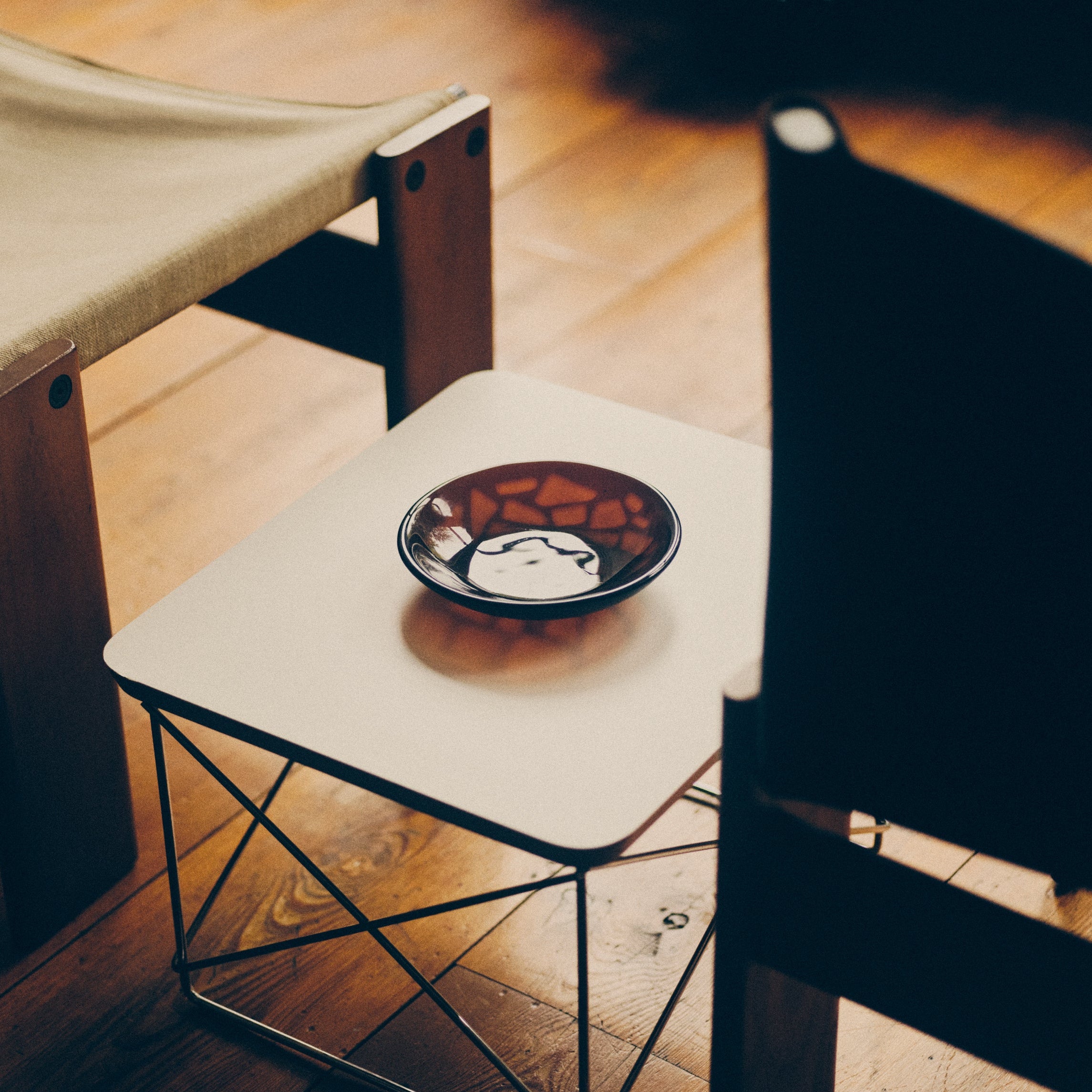 Dark amber glass bowl by Savoia Everything sat on a low white table between two chairs on a wooden floor.