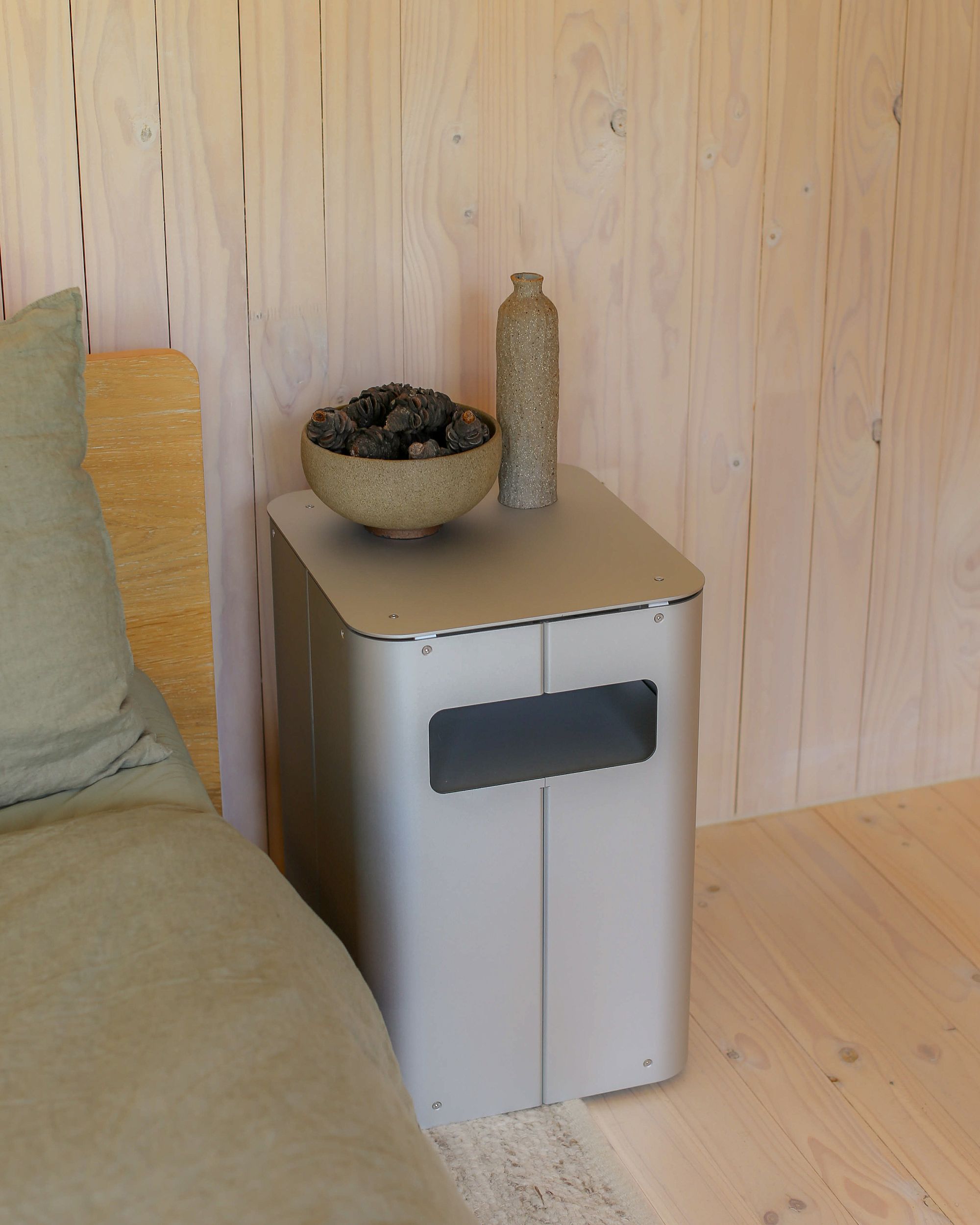 Bedside table by PARCTA placed besides a bed with green linen in a wooden cabin.