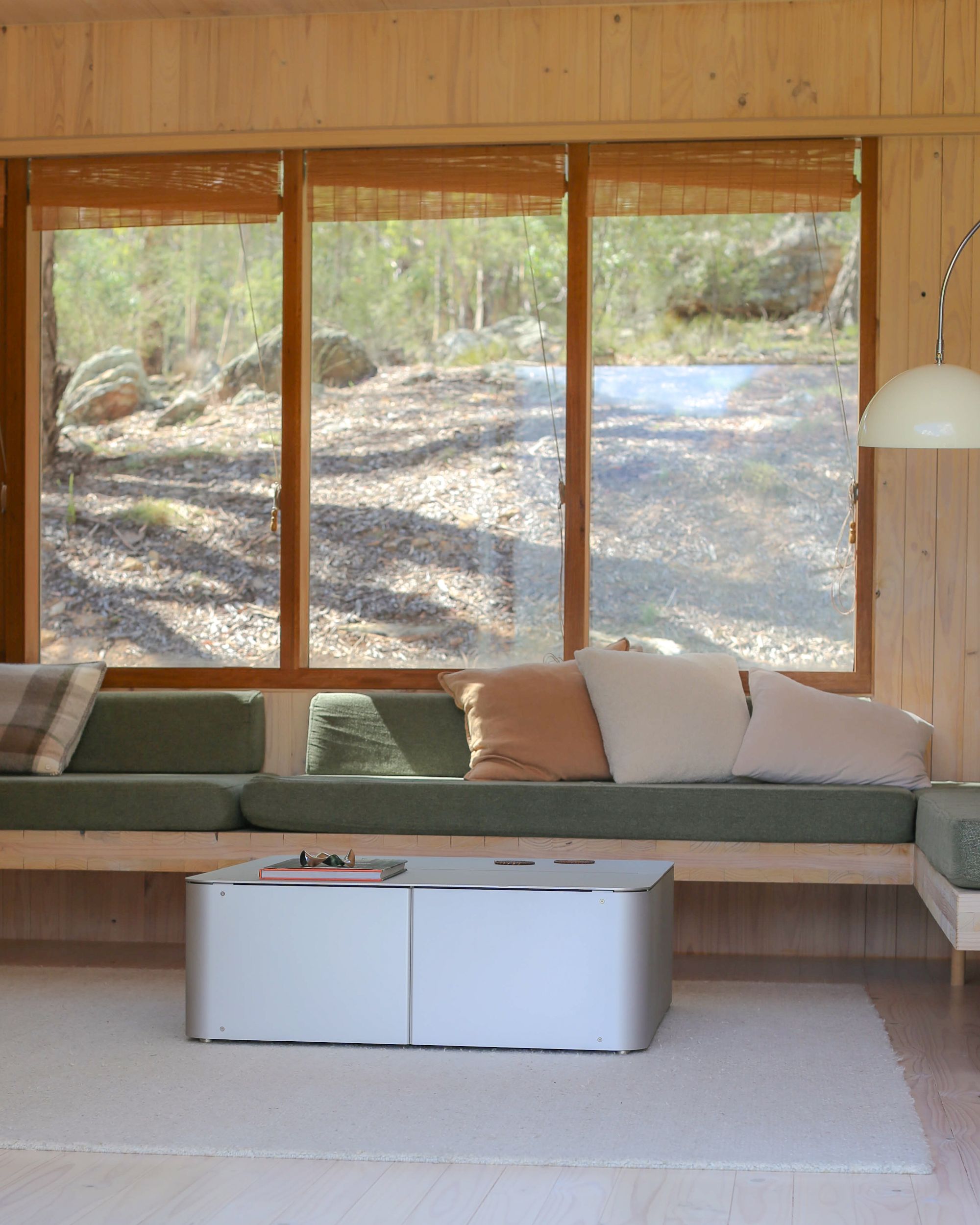 Coffee Table by PARCTA in a living area in a wood cabin on a neutral rug with a green sofa. There's large windows in the background showing woodland.
