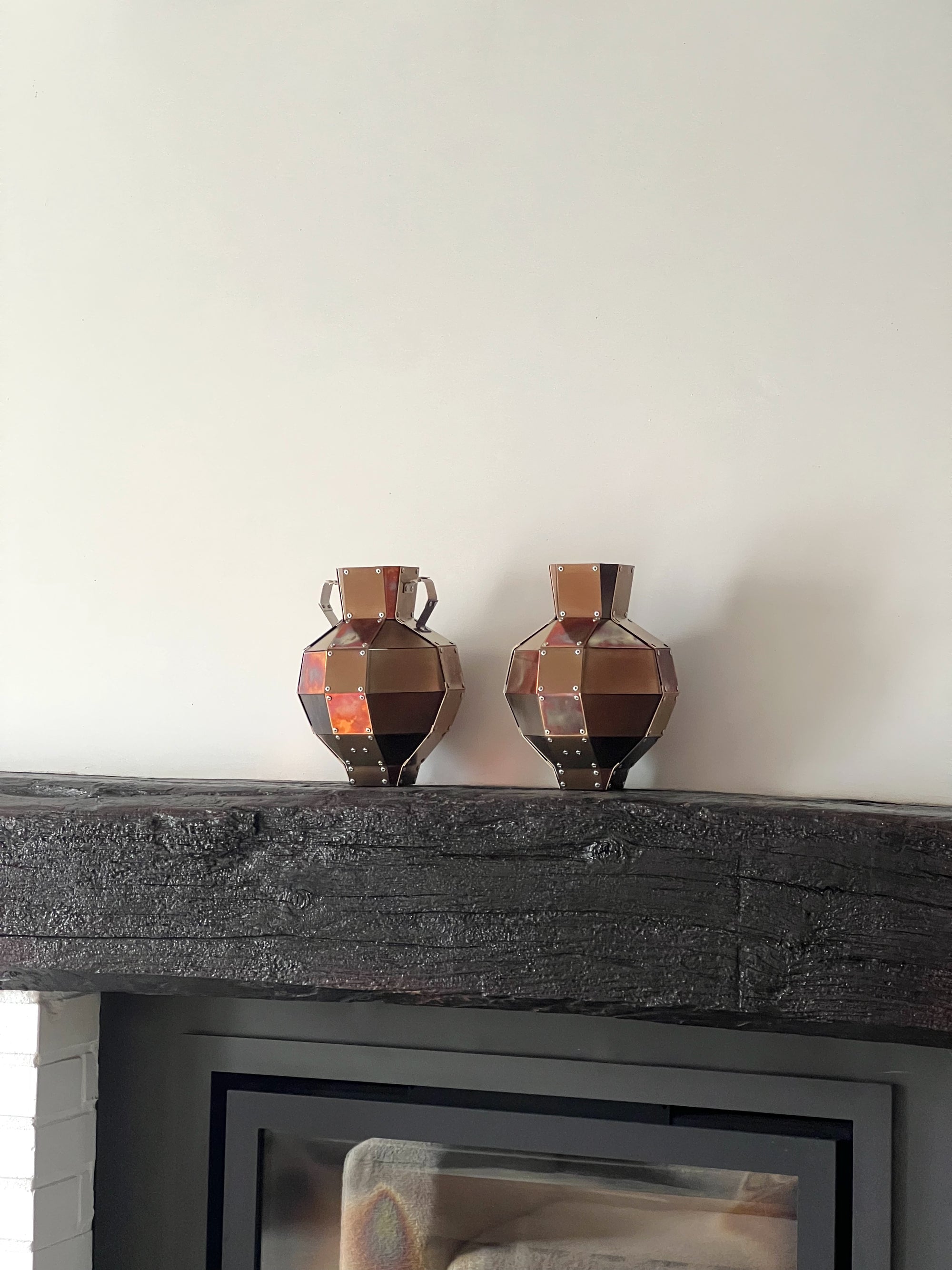 Two stainless steel and copper decorative objects by Theo Galliakis sat on top of a fire place.