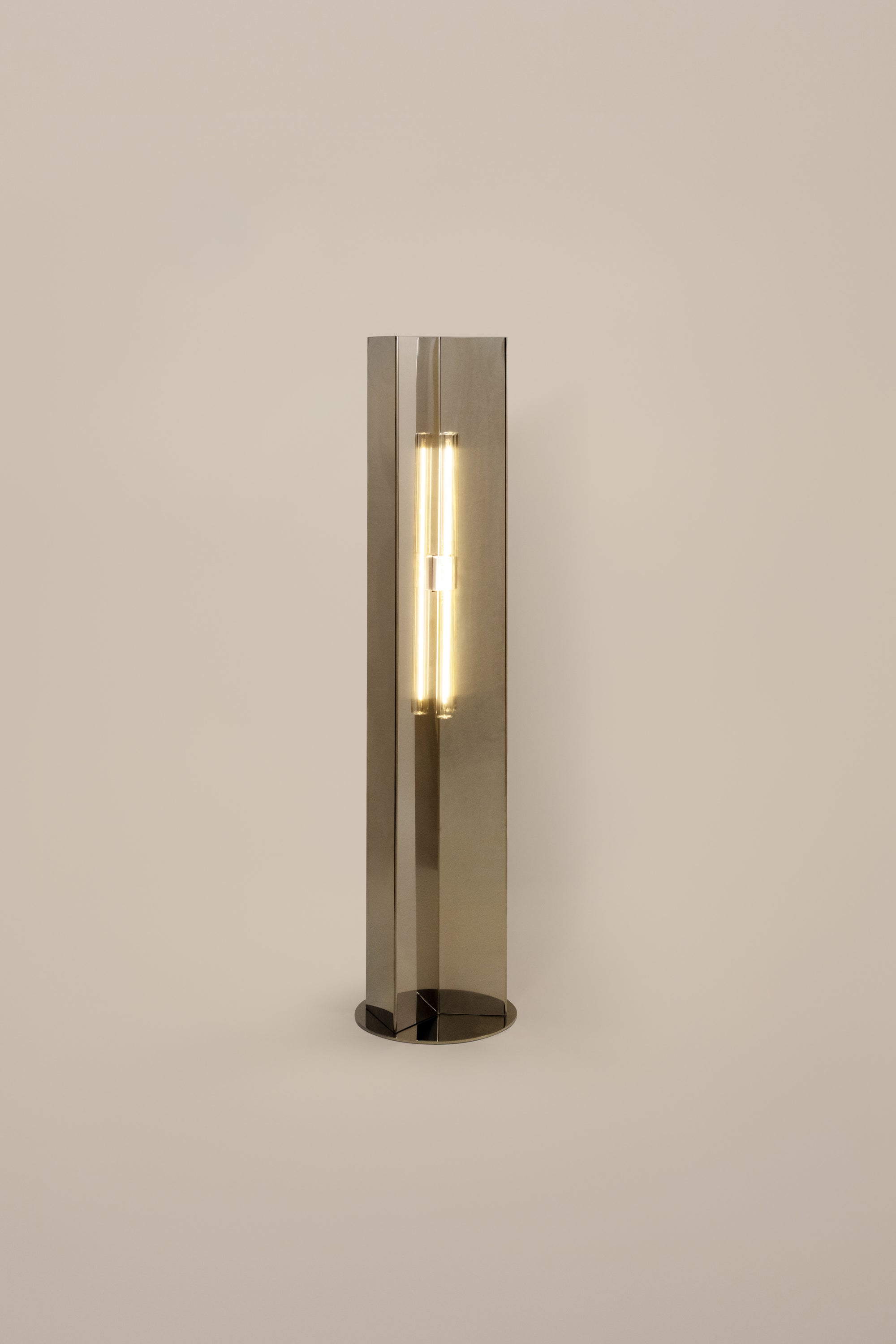 Polished steel foot lamp by Violaine d'Harcourt on a neutral background with light on.