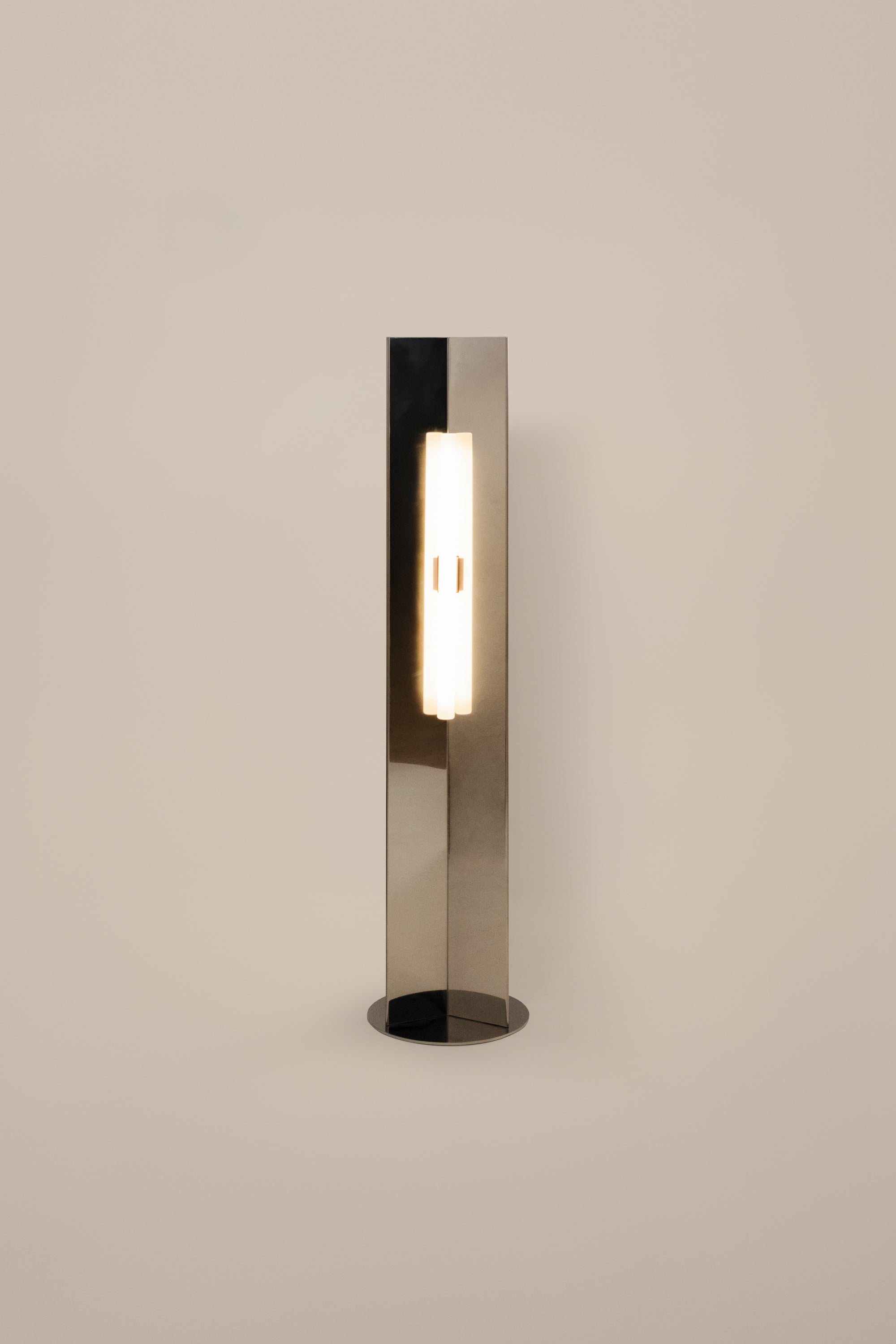 Polished steel foot lamp by Violaine d'Harcourt on a neutral background with light on.