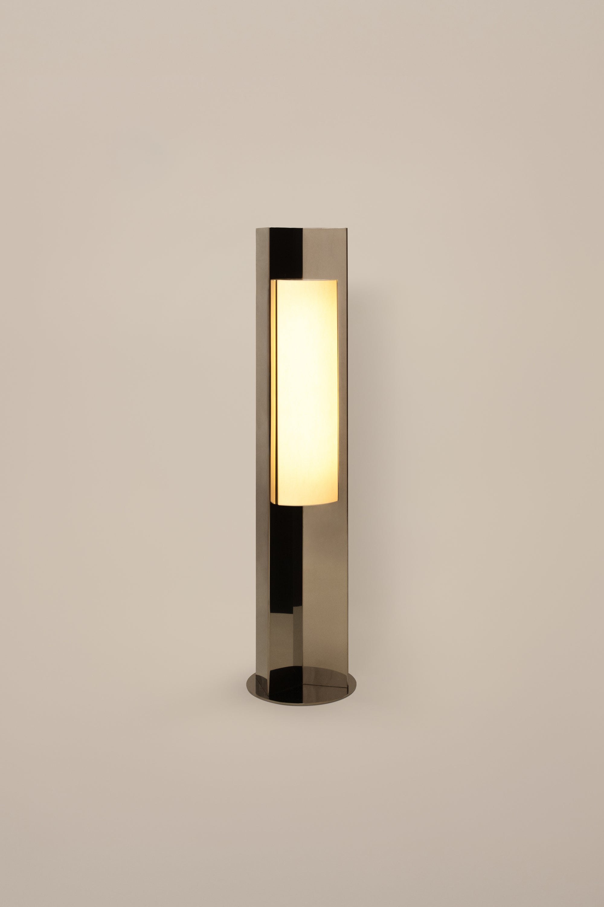 Polished steel foot lamp with paper diffuser by Violaine d'Harcourt on a white background with light on.
