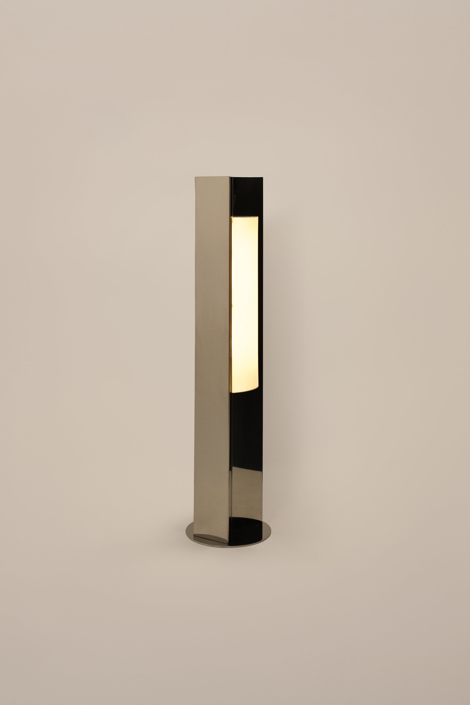Polished steel foot lamp with paper diffuser by Violaine d'Harcourt on a neutral background with light on.