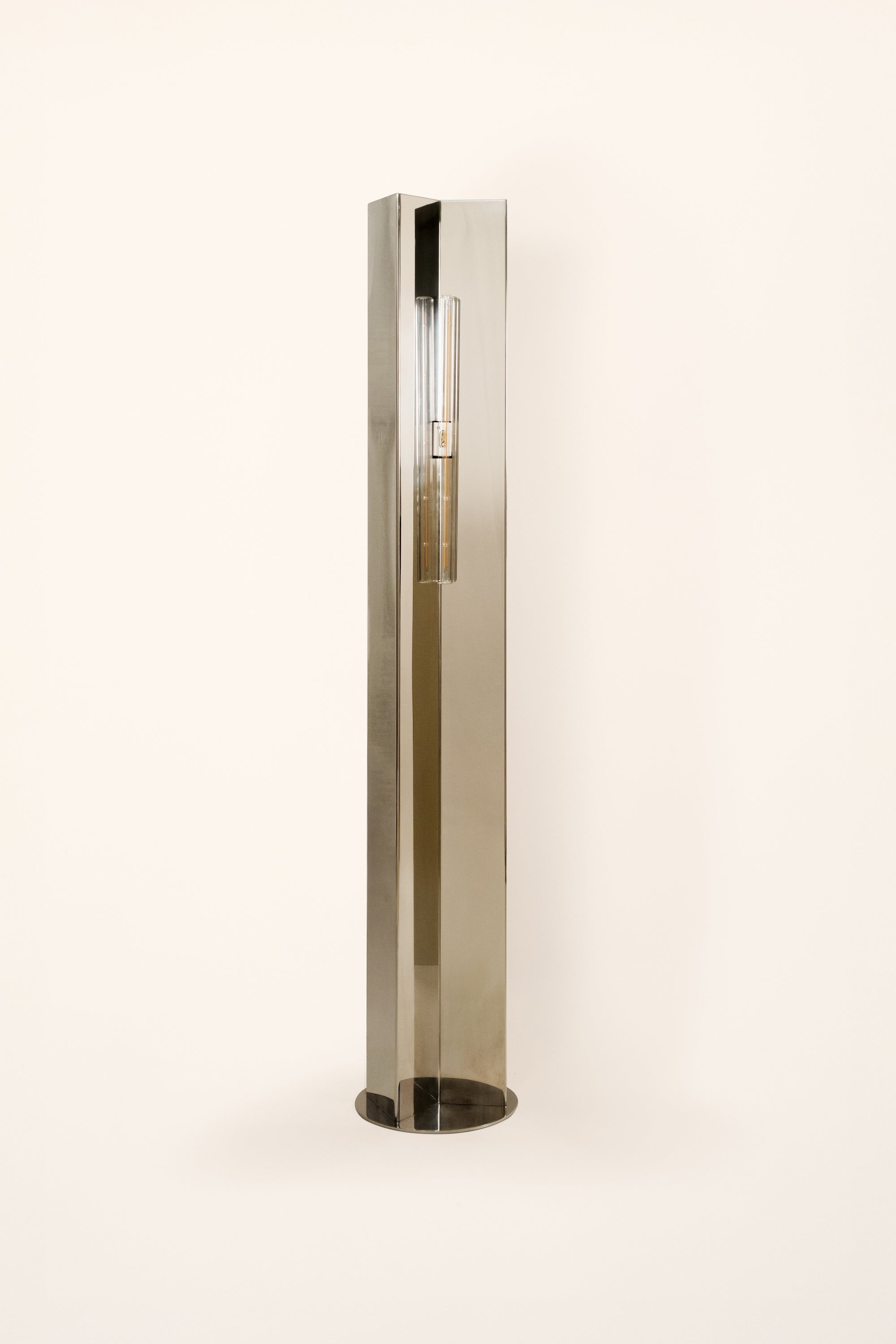 Polished steel foot lamp by Violaine d'Harcourt on a white background with light off.