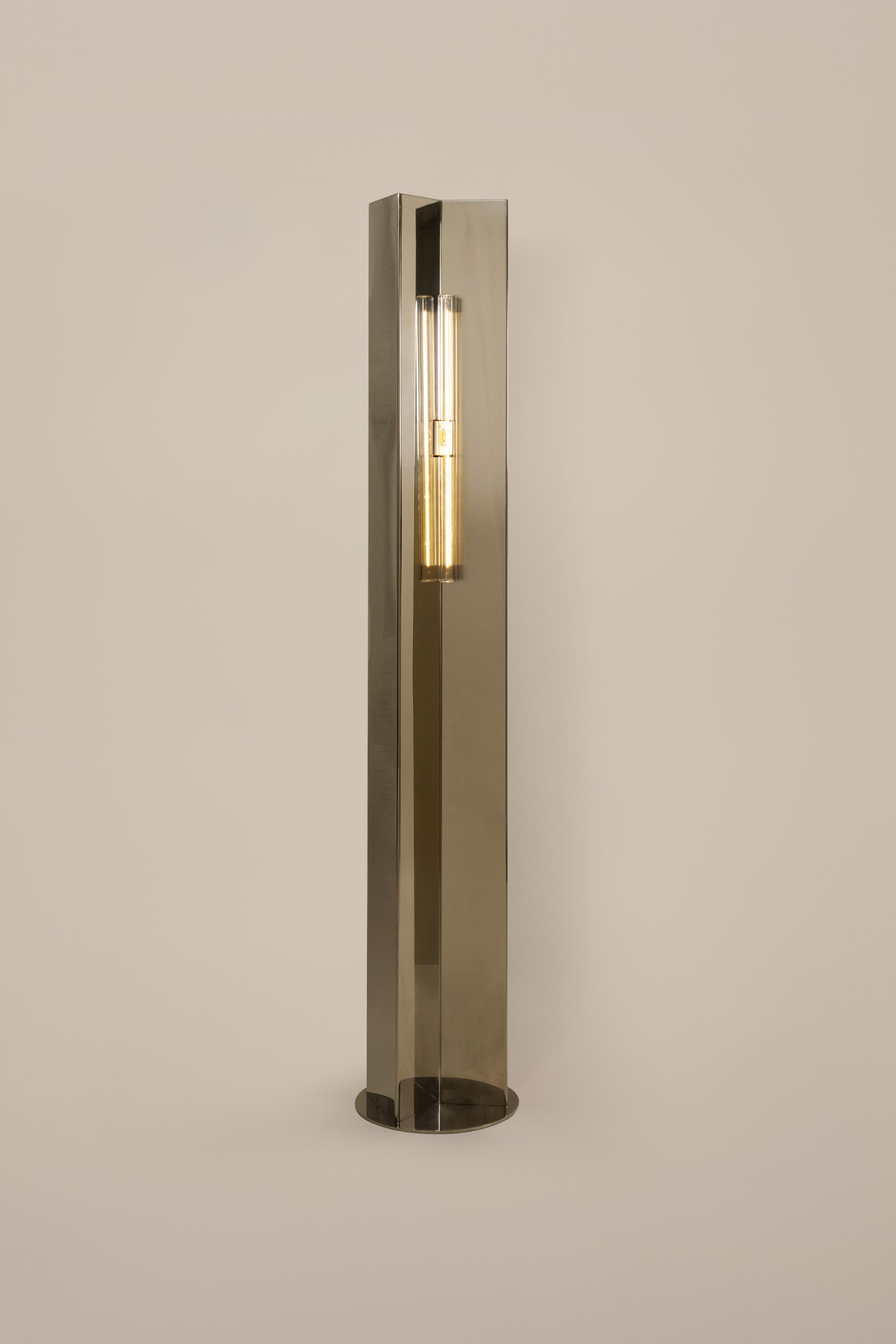Polished steel foot lamp by Violaine d'Harcourt on a neutral background with light on.