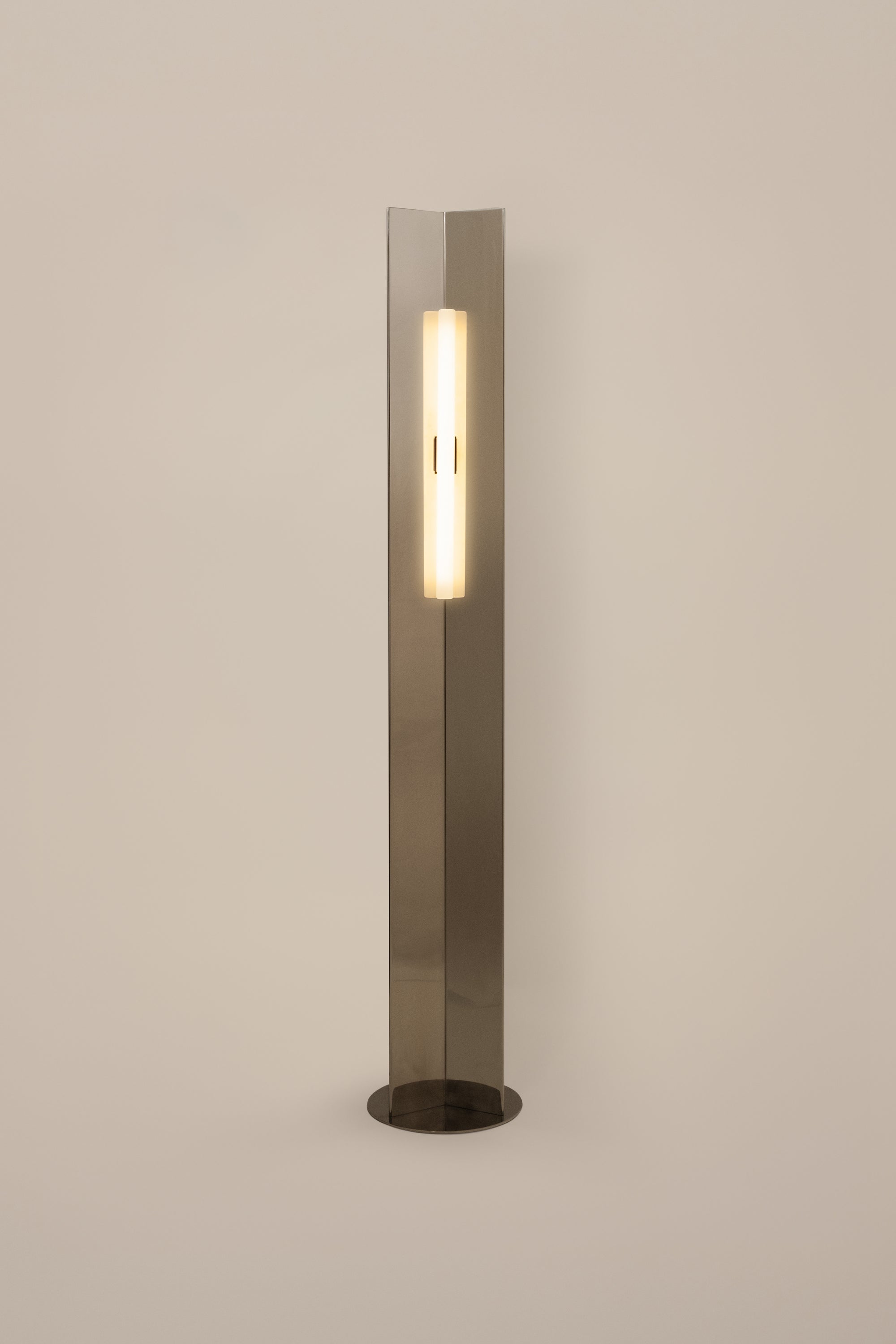 Polished steel foot lamp by Violaine d'Harcourt on a neutral background with light on.