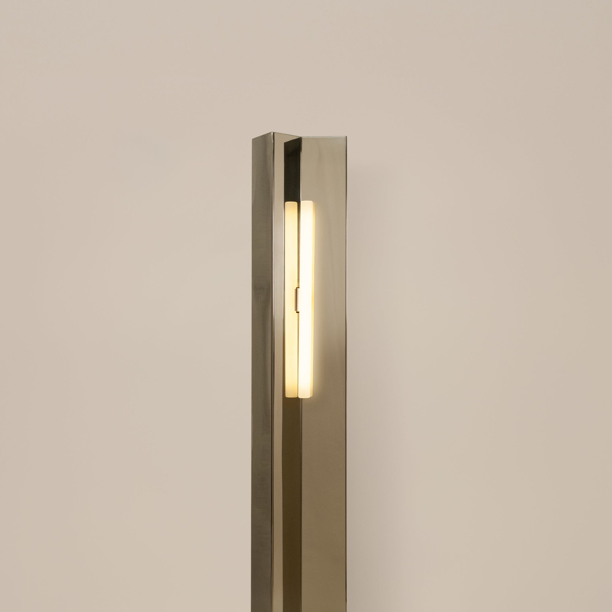 Polished steel foot lamp by Violaine d'Harcourt on a neutral background with light on.