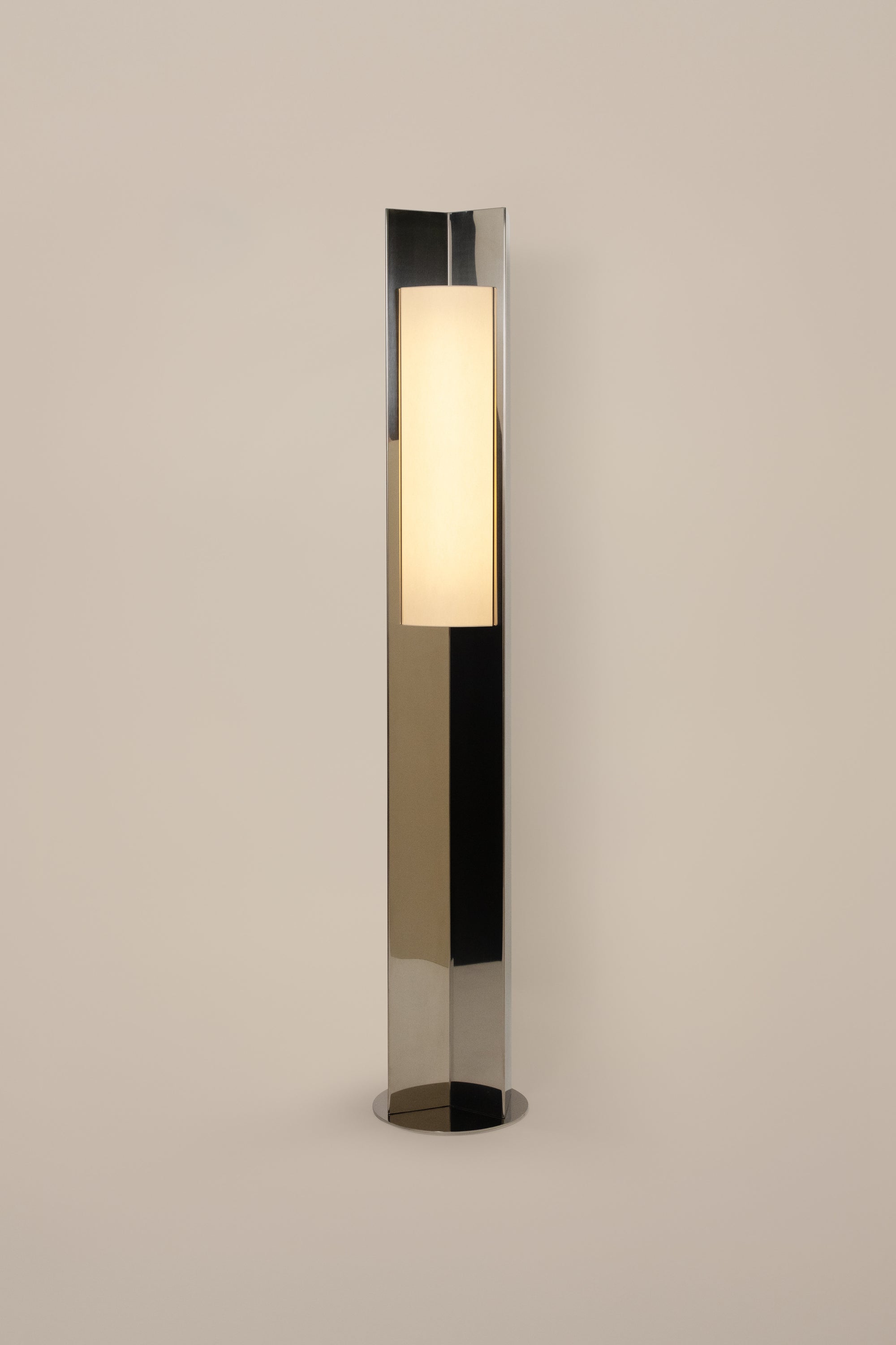 Polished steel foot lamp with paper diffuser by Violaine d'Harcourt on a neutral background with light on.