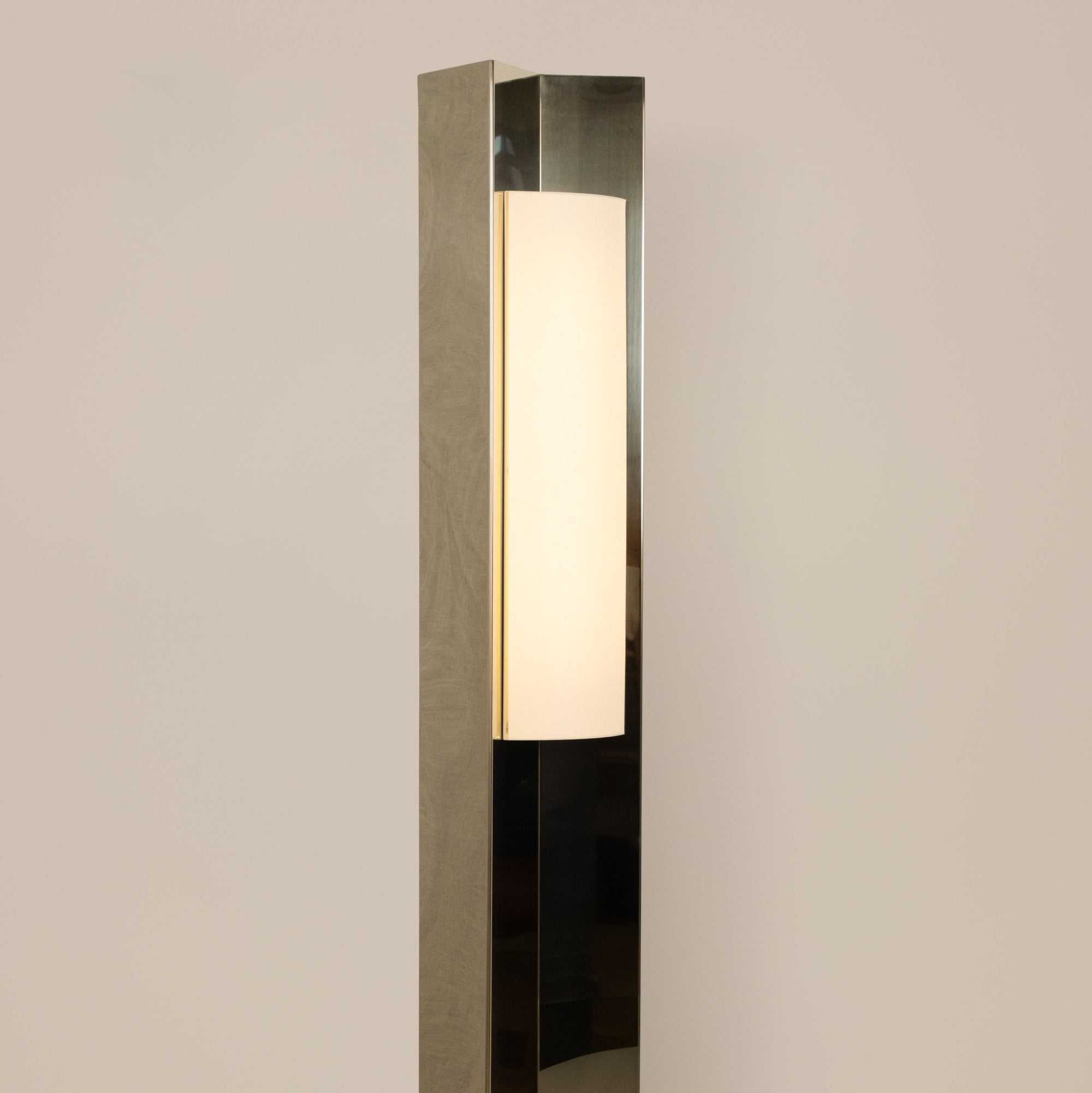 Polished steel foot lamp with paper diffuser by Violaine d'Harcourt on a neutral background with light on.