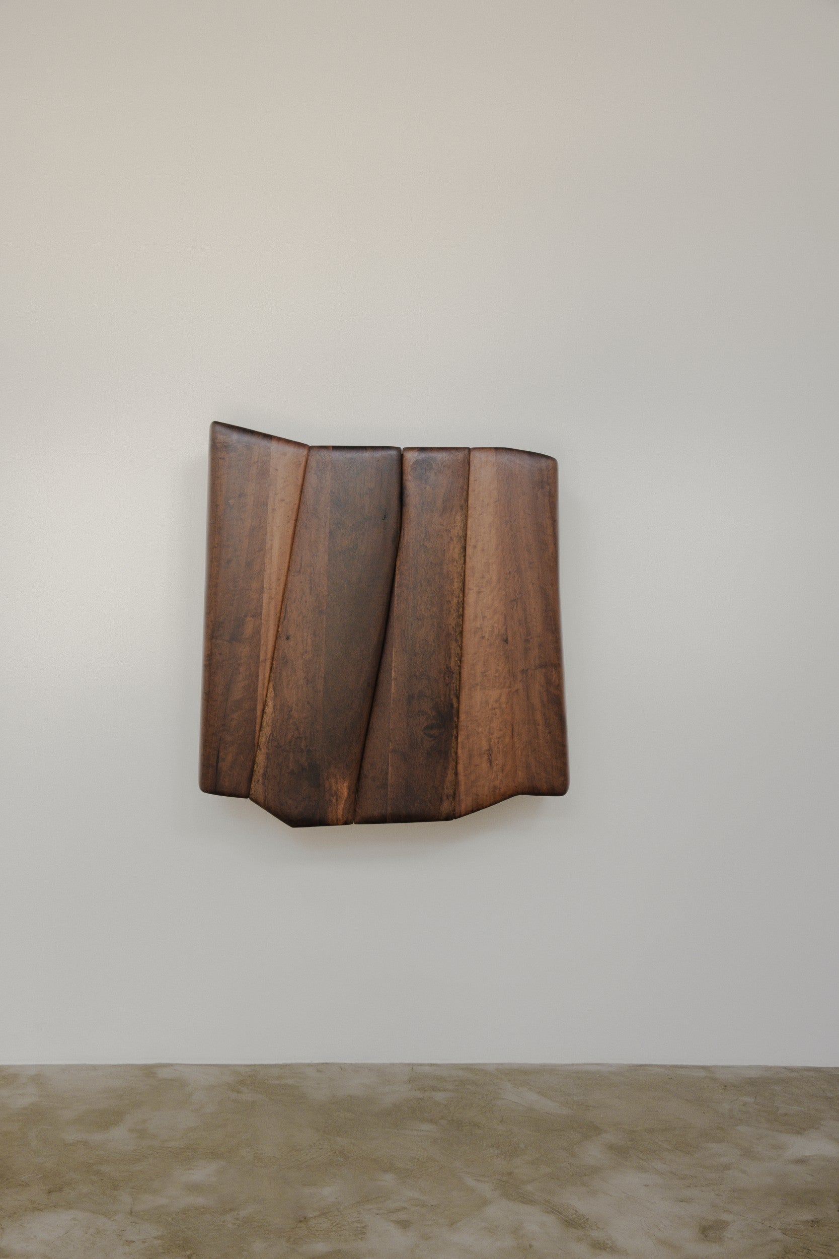 Wooden wall mounted cabinet by Estudio Prosa with both doors closed, on a neutral background with concrete floor.