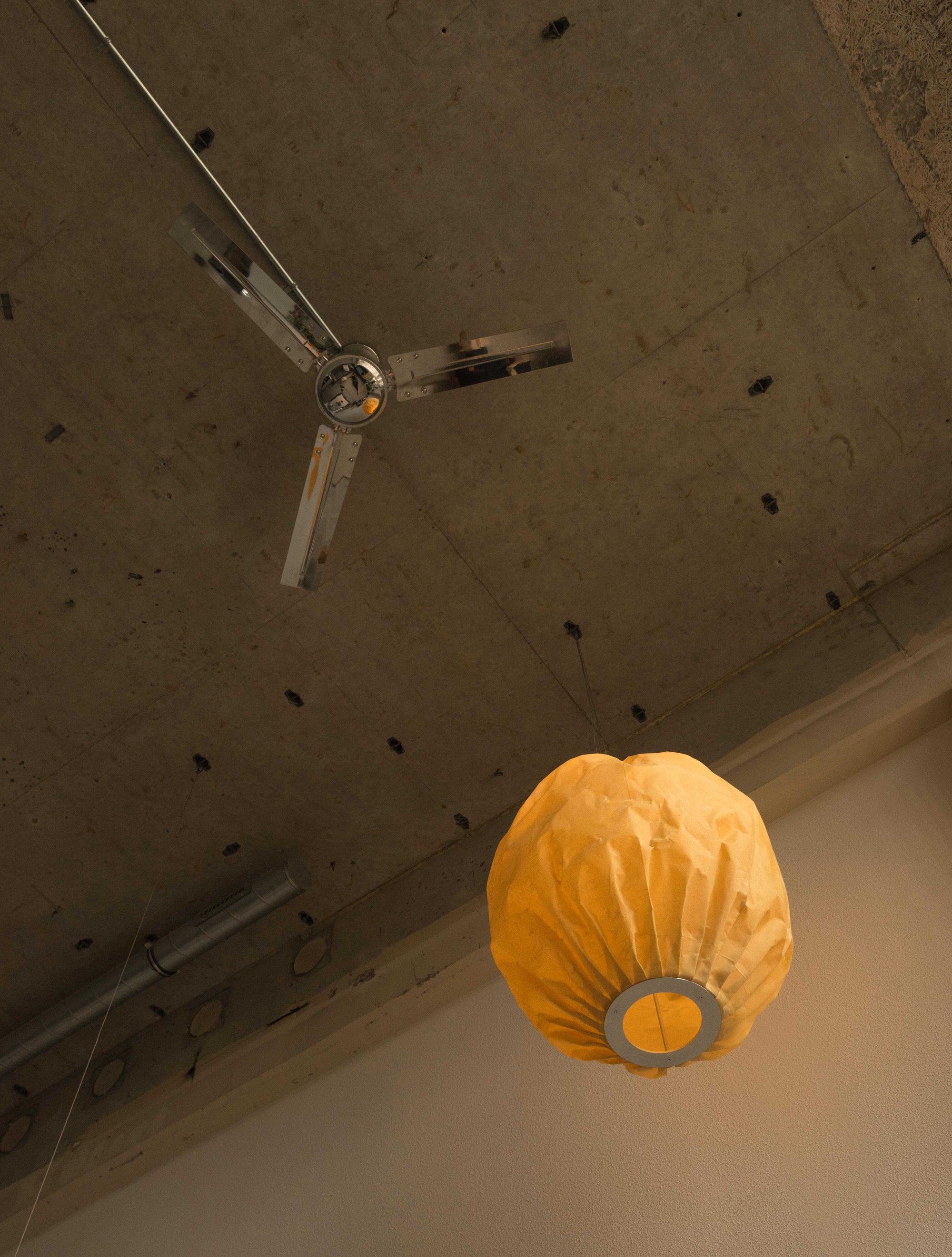 Beeswax Bubble Colmena Pendant light by Pablo Bolumar hanging from the industrial ceiling besides a stainless steel fan.