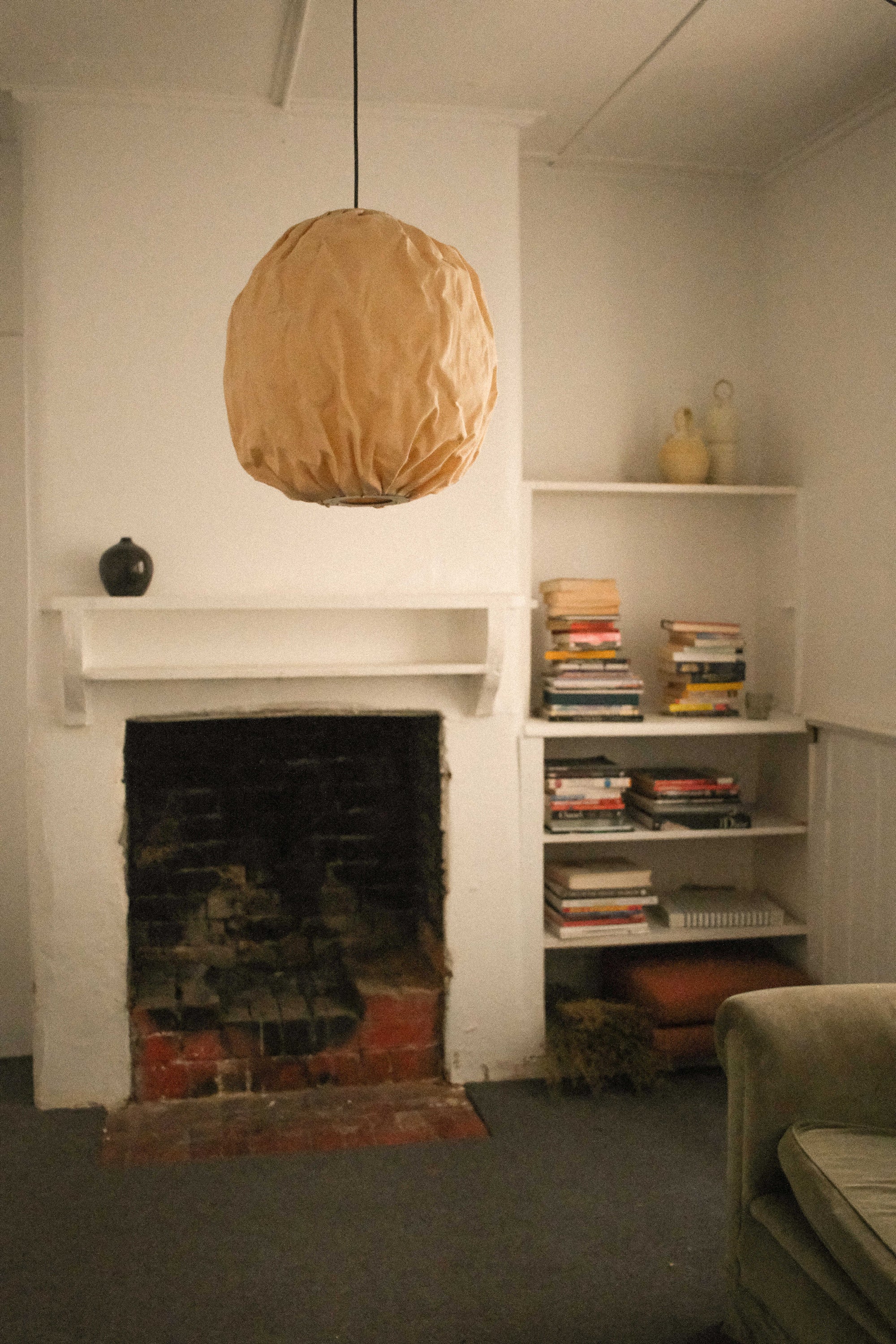 Living room with a fireplace, bookshelf, and Beeswax Bubble Colmena Pendant light by Pablo Bolumar hanging from the ceiling.