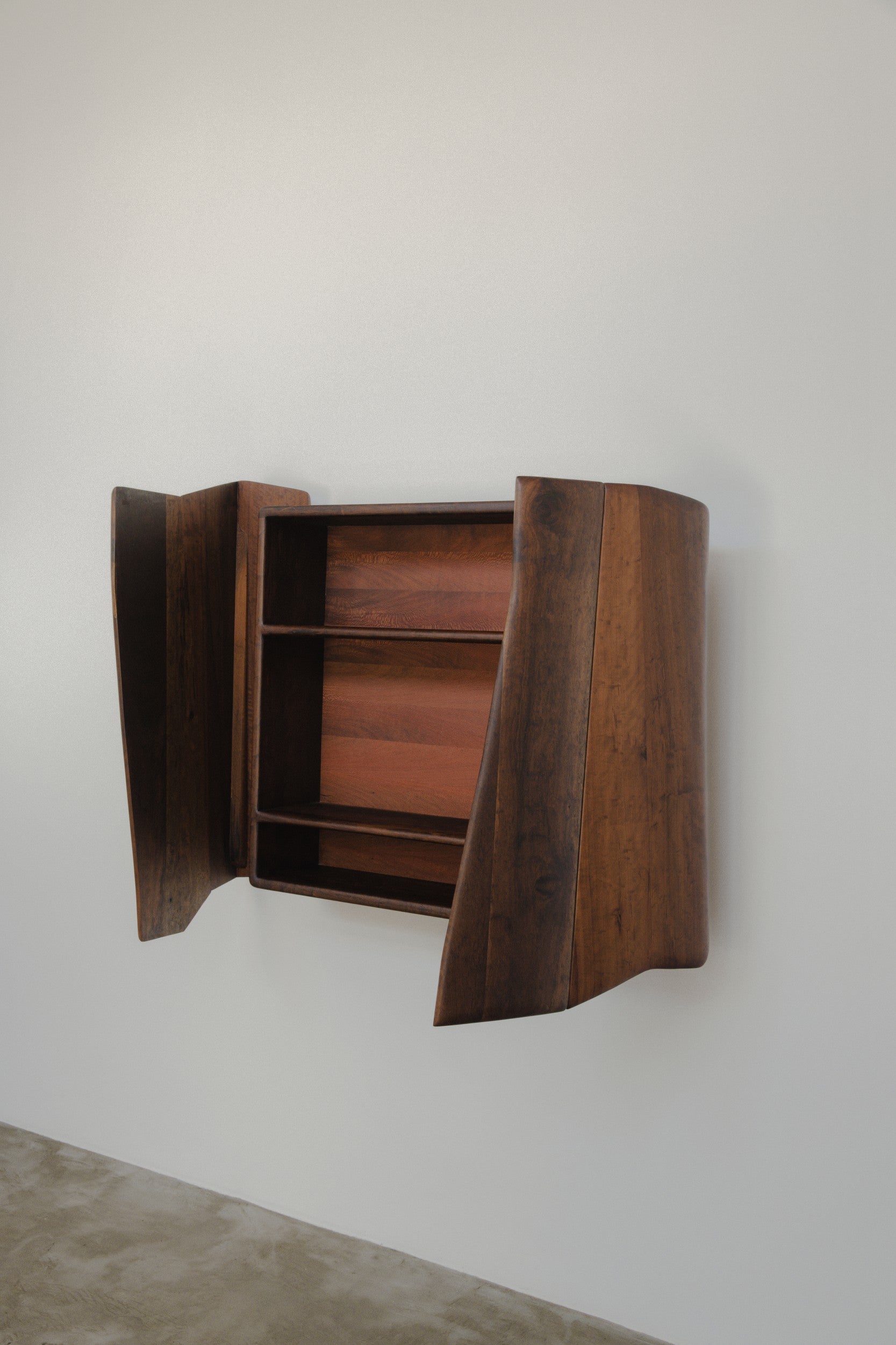 Wooden wall mounted cabinet by Estudio Prosa with both doors open, on a neutral background with concrete floor.