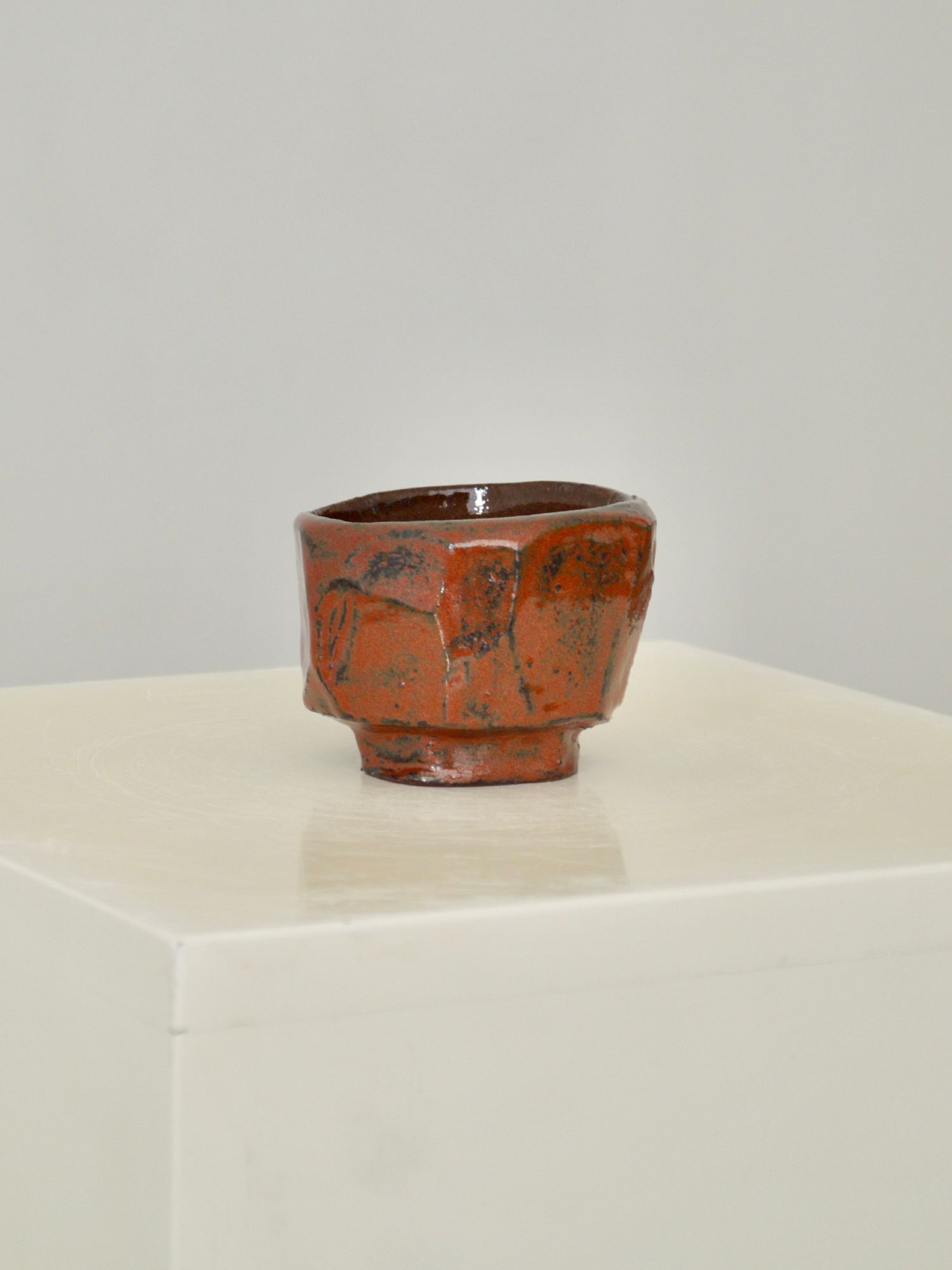 A ruby coloured coffee cup by Zeynep Boyan on white plinth with a neutral background.