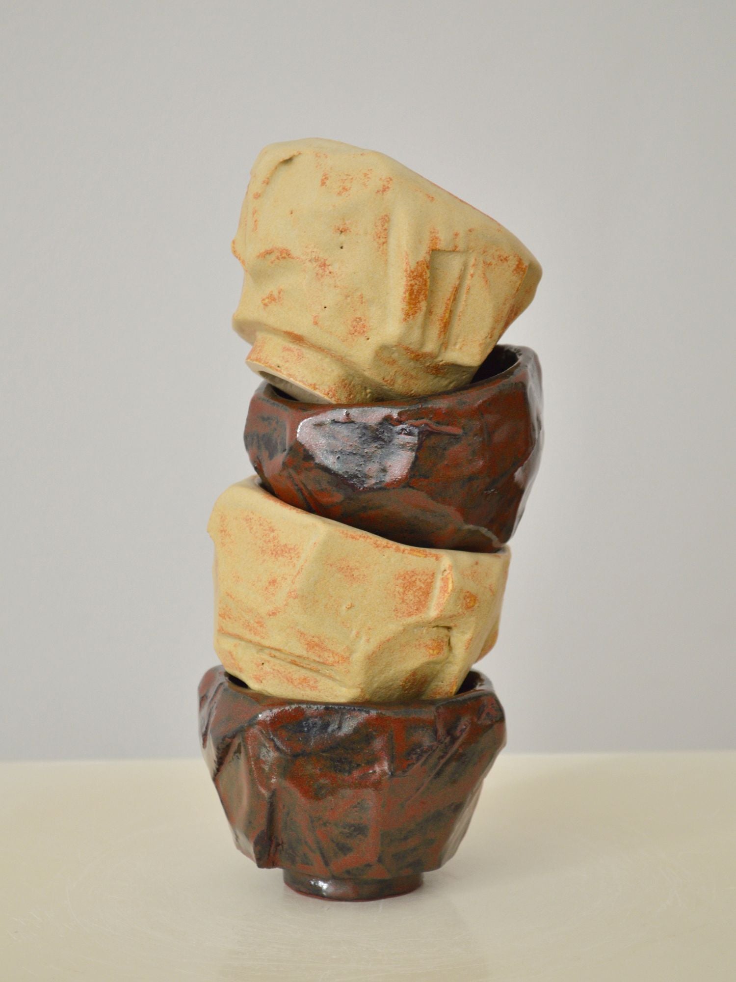 An alternating stack of four sand and ruby coloured coffee cups by Zeynep Boyan on a neutral background.