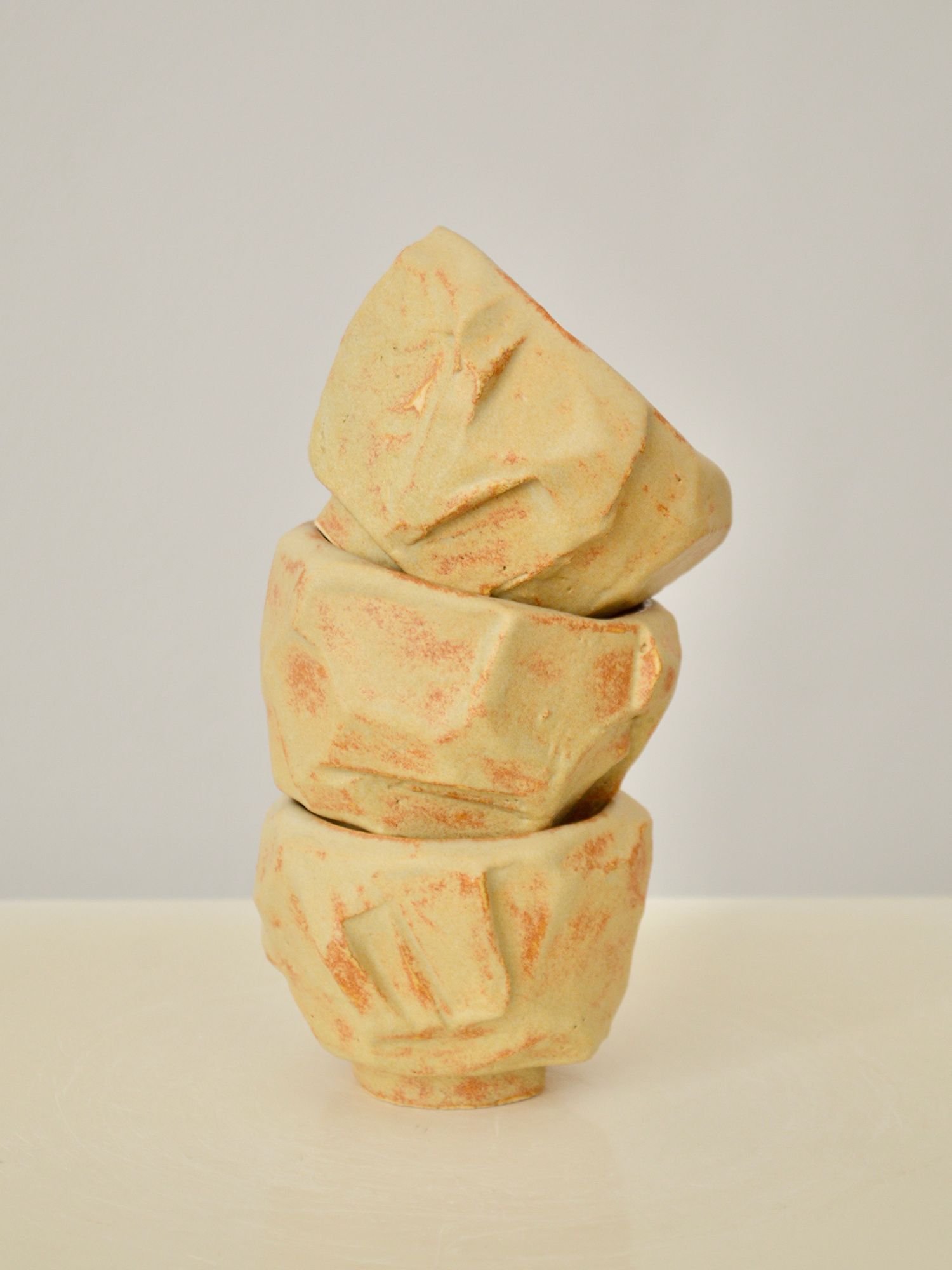 A stack of three sand coloured coffee cups by Zeynep Boyan on a neutral background.