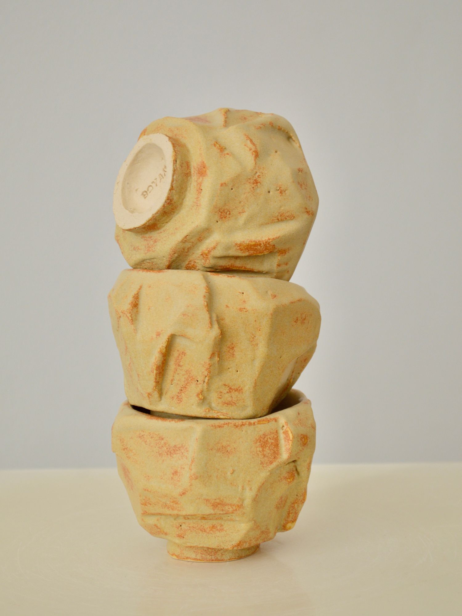 A stack of three sand coloured coffee cups by Zeynep Boyan on a neutral background. The top cup is tilted featuring Boyan engraved on the base.