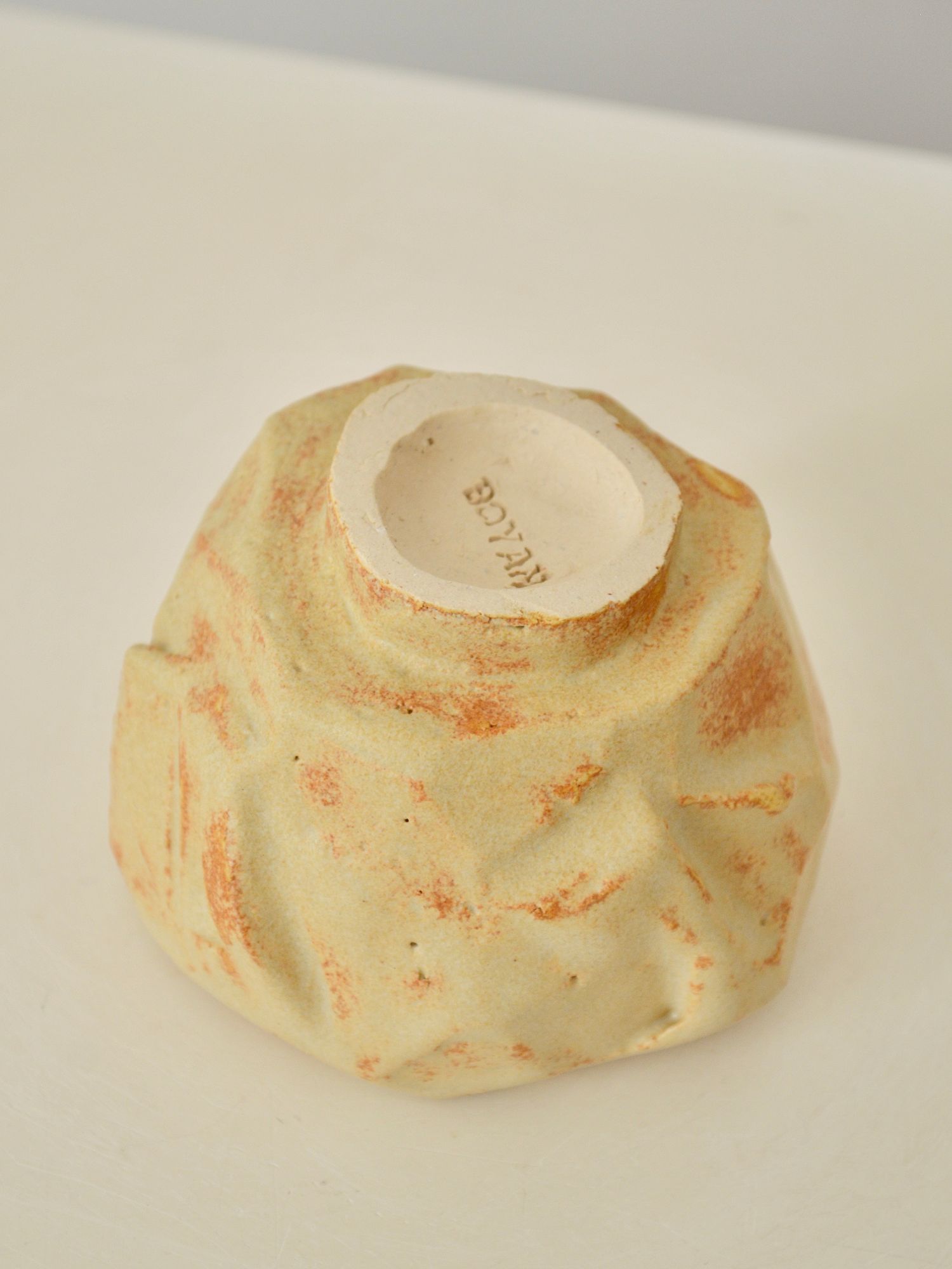 The bottom of a sand coloured coffee cup by Zeynep Boyan, featuring Boyan engraved on the base, set against a neutral background.